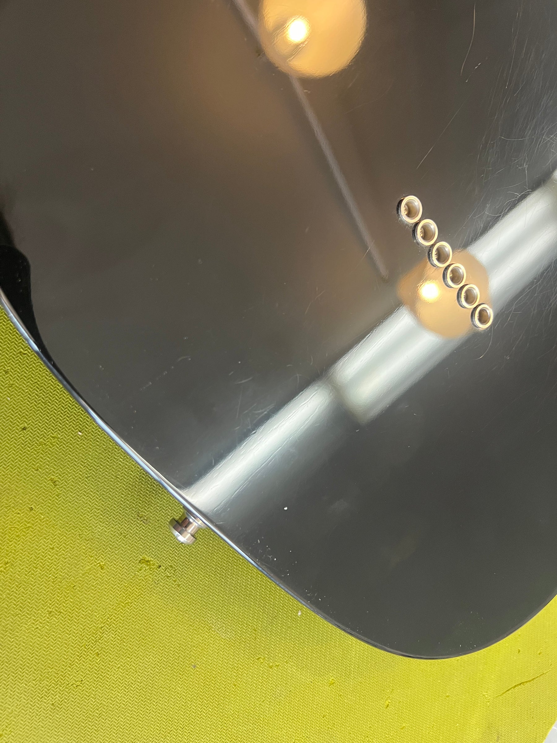 The black guitar body's lower bout shows six gold string ferrules, a strap button, and light surface scratches.