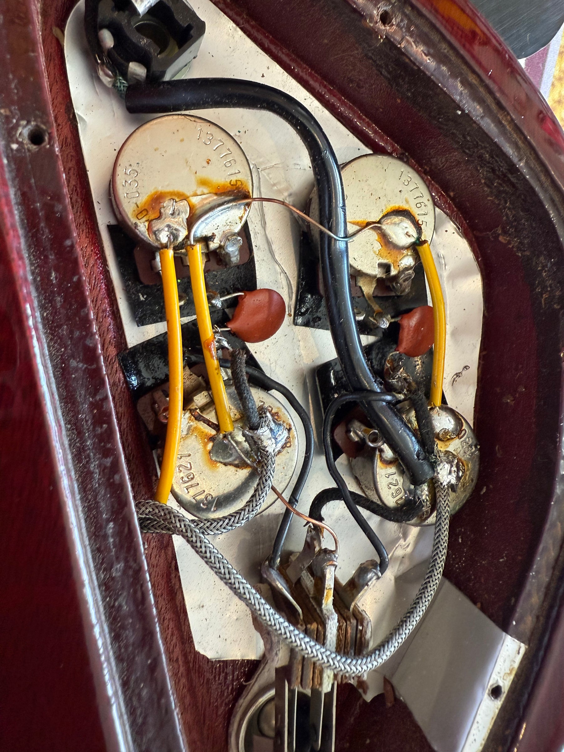 Close-up of the guitar's control cavity, revealing four pots, orange capacitors, and wiring with some corrosion visible.