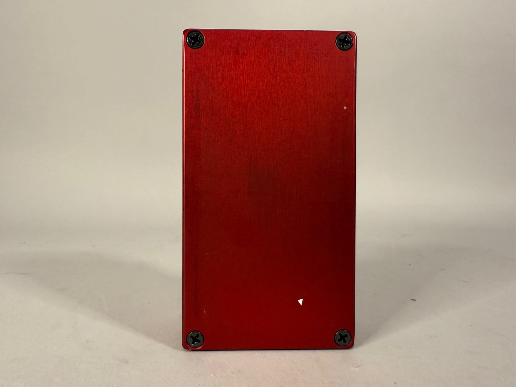 The red brushed metal pedal is viewed from the back, showing four black Phillips head screws and a small white scuff.