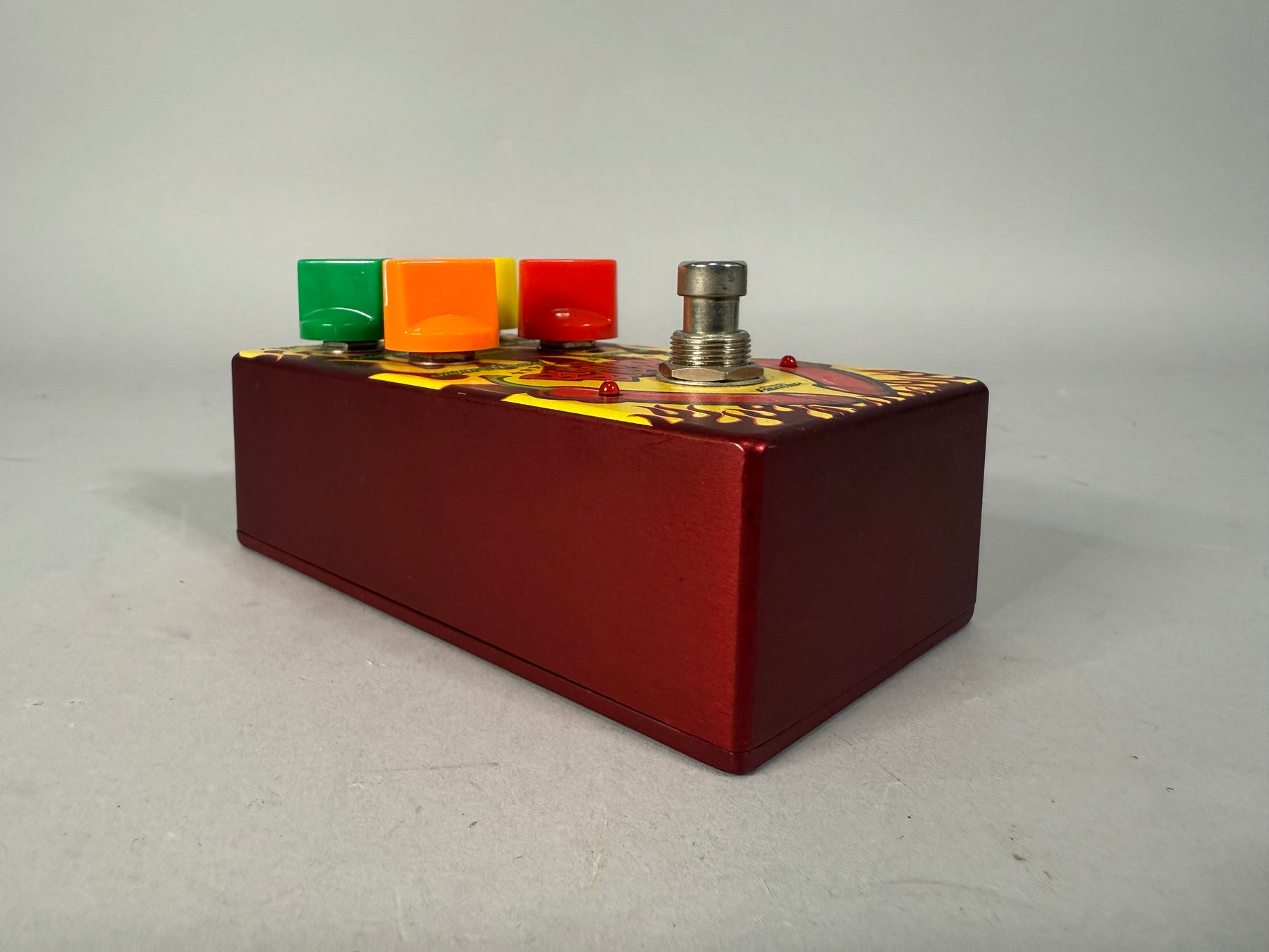 Red guitar pedal with a yellow and red graphic top, four colorful knobs, and a silver footswitch.