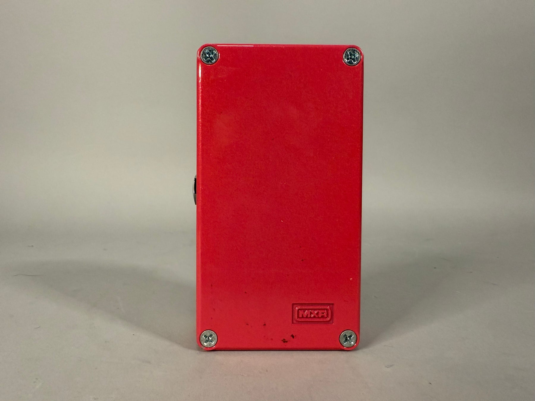 The red pedal is viewed from the back, showing four silver screws and a small black button on the left side.