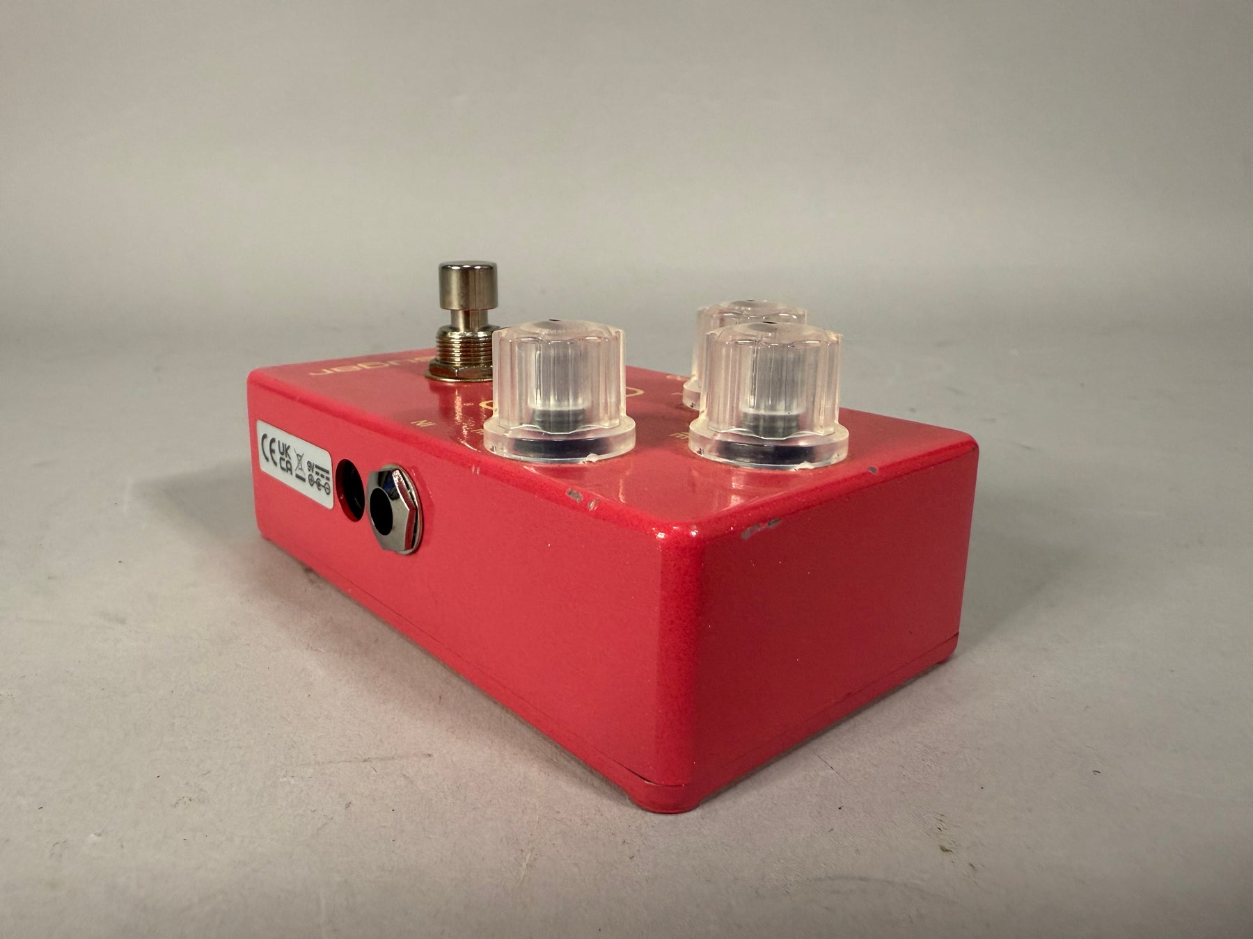 A red guitar pedal with three clear knobs, a metal footswitch, and an input jack on the left side.