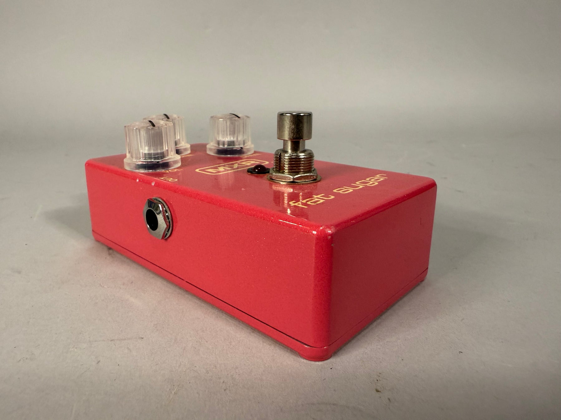 The red metallic pedal is angled right, showing the input jack, three clear knobs, and a footswitch, with some paint chips.