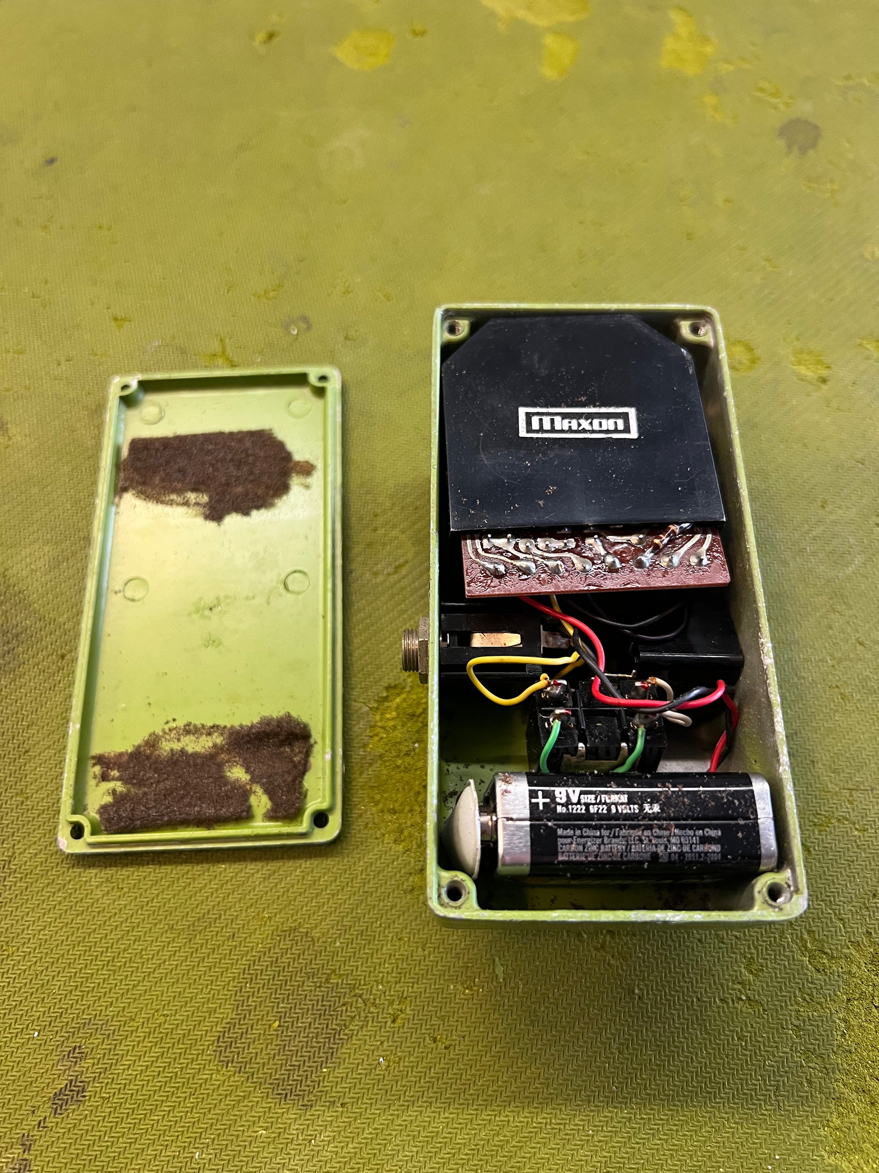 The light green pedal's bottom plate is removed, revealing internal wiring, a circuit board, and a 9V battery.