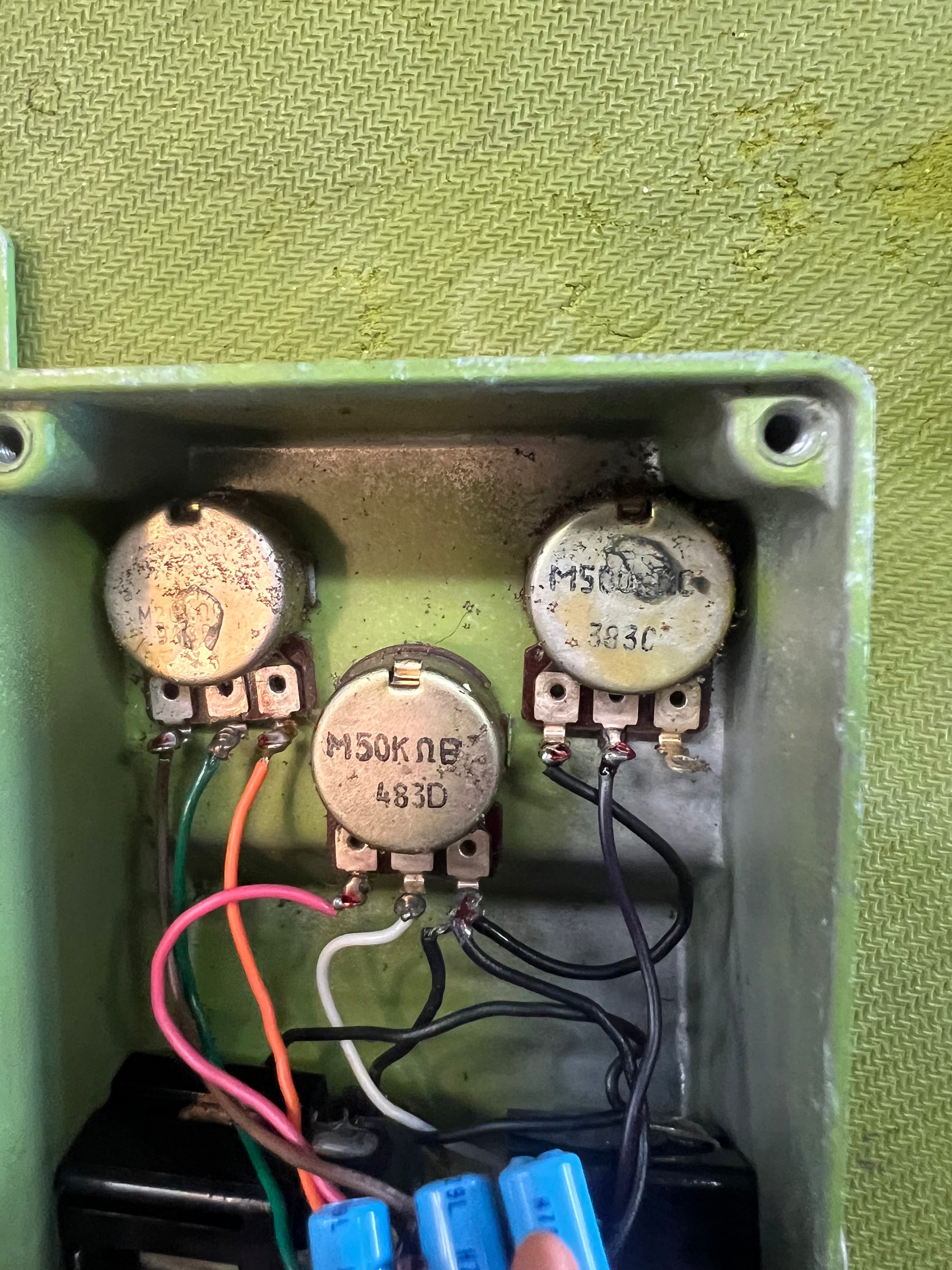 An overhead view of the pedal's light green interior, revealing three tarnished potentiometers with soldered wires and blue capacitors below.