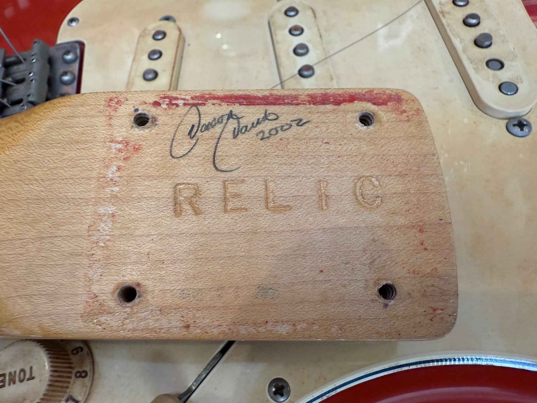 Close-up of the guitar's neck heel, showing "RELIC" carved into the wood, a signature, and red finish wear.