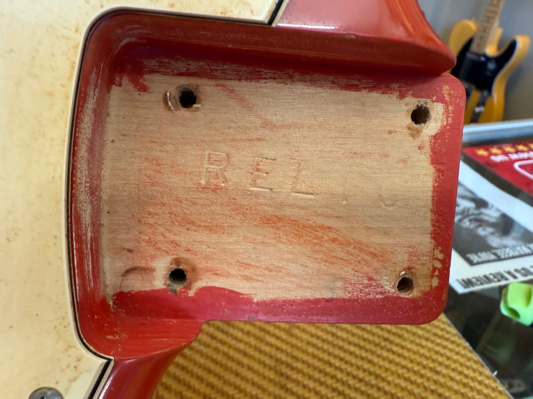 Close-up of the guitar's neck pocket, showing exposed wood with red paint residue and four screw holes.