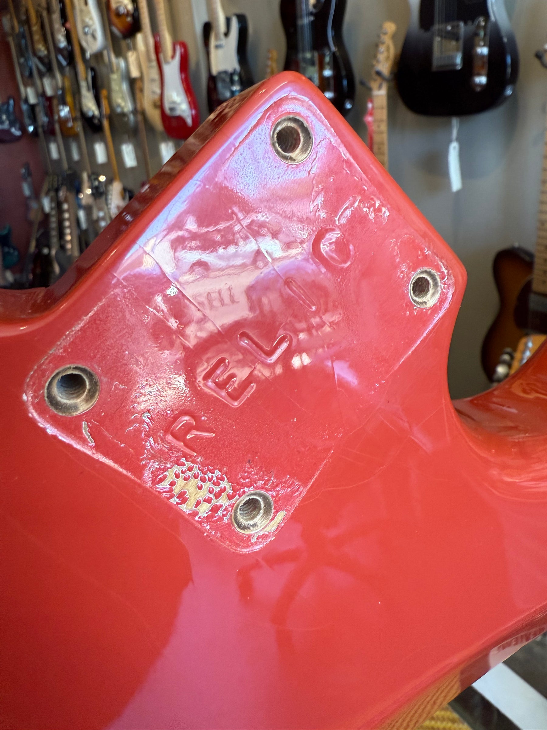 Close-up of the Fiesta Red body's neck pocket, showing four screw holes, heavy finish wear, and visible checking.