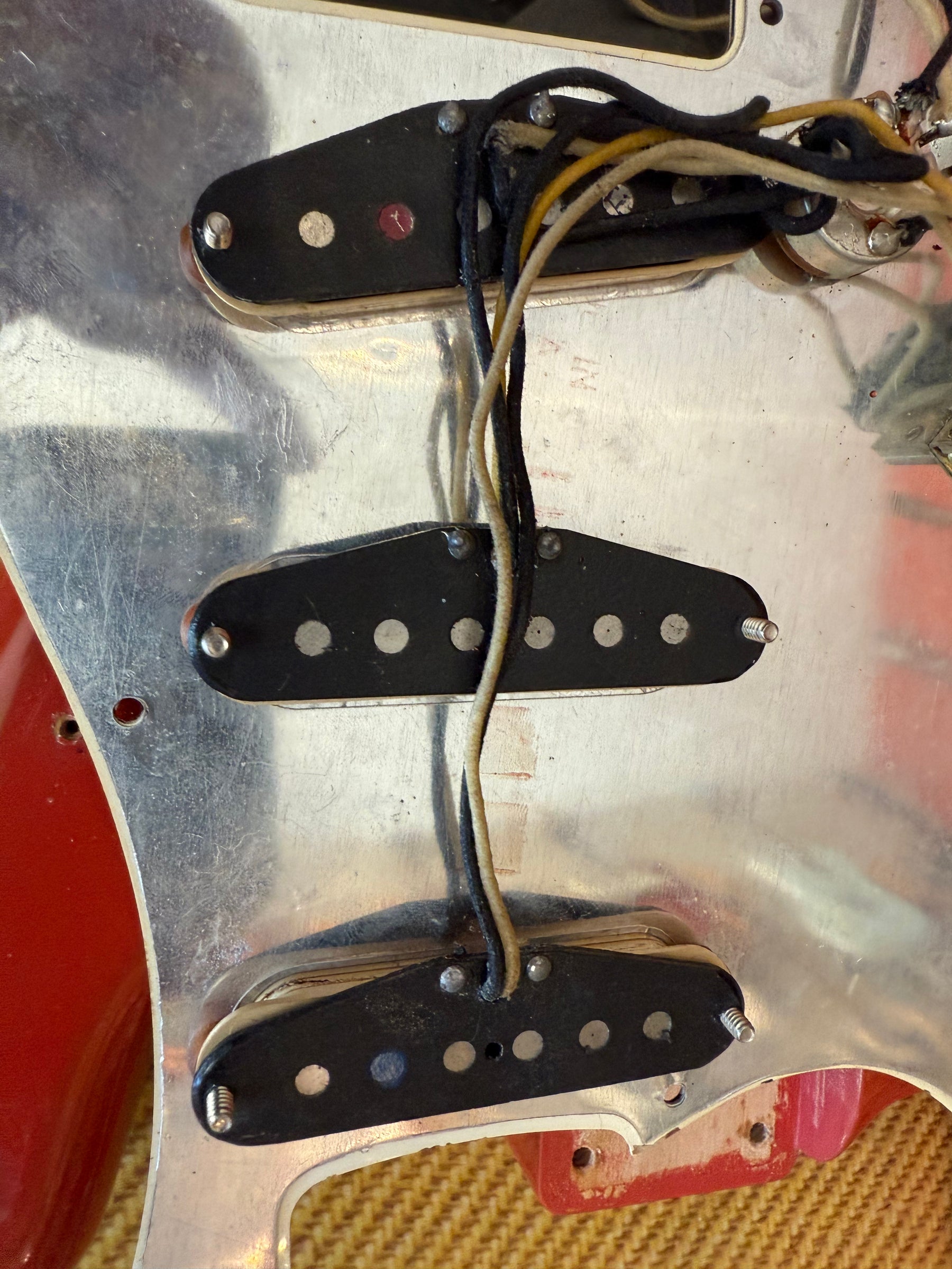 Close-up of the guitar's wiring, showing three single-coil pickups with black covers and exposed pole pieces on a scratched aluminum pickguard.