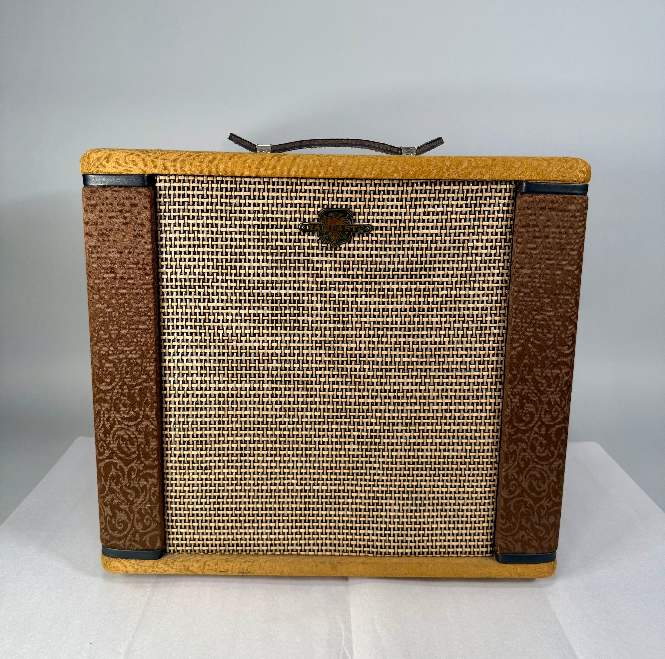 Front view of a brown and tan combo amp with a woven grille, ornate brown side panels, and a dark leather handle.