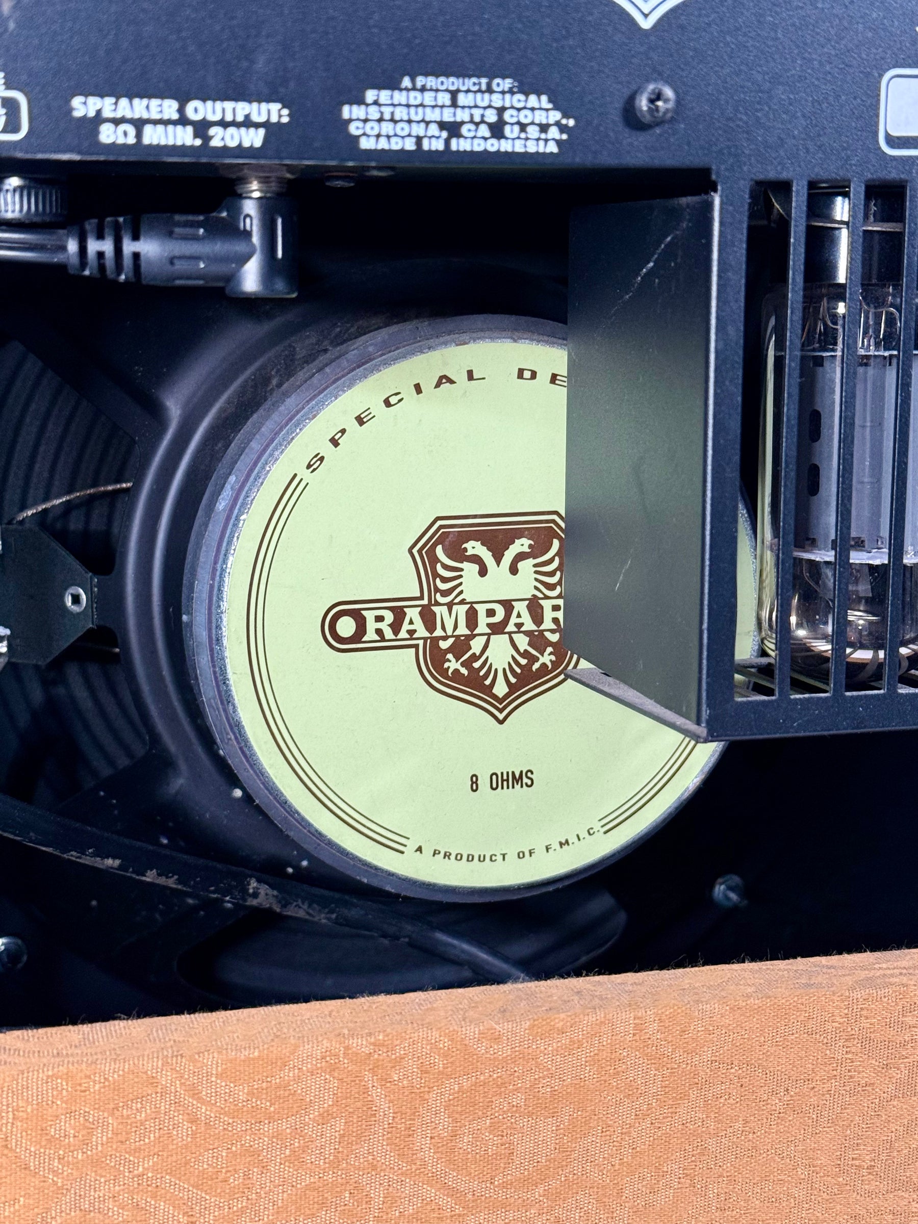 Close-up of the amplifier's rear, showing the speaker cone with a light green label, tubes, and orange patterned grille cloth.