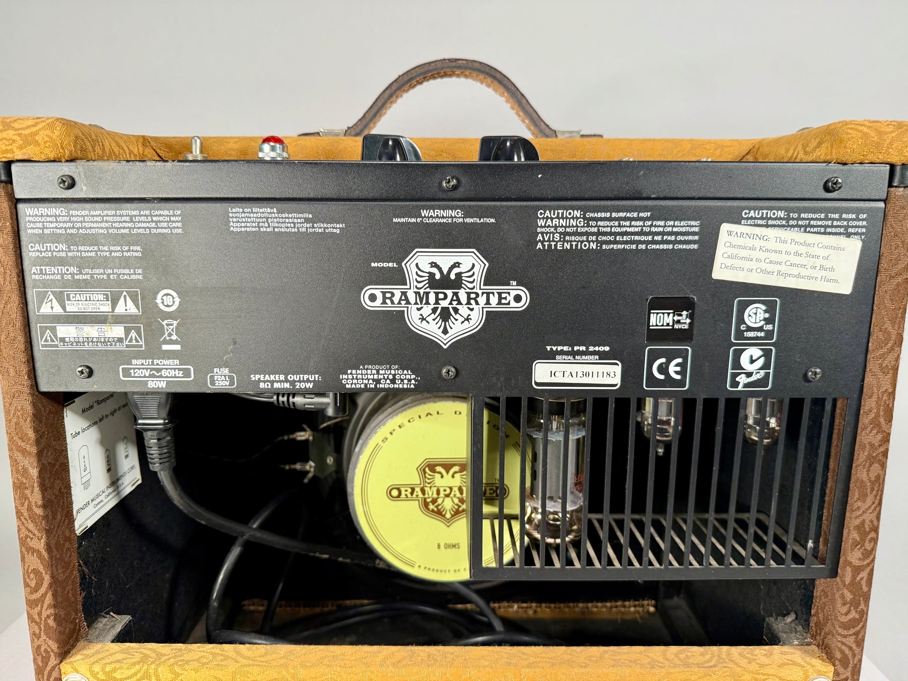 Rear view of a brown and gold patterned combo amp, showing the black control panel, exposed tubes, and power cord.