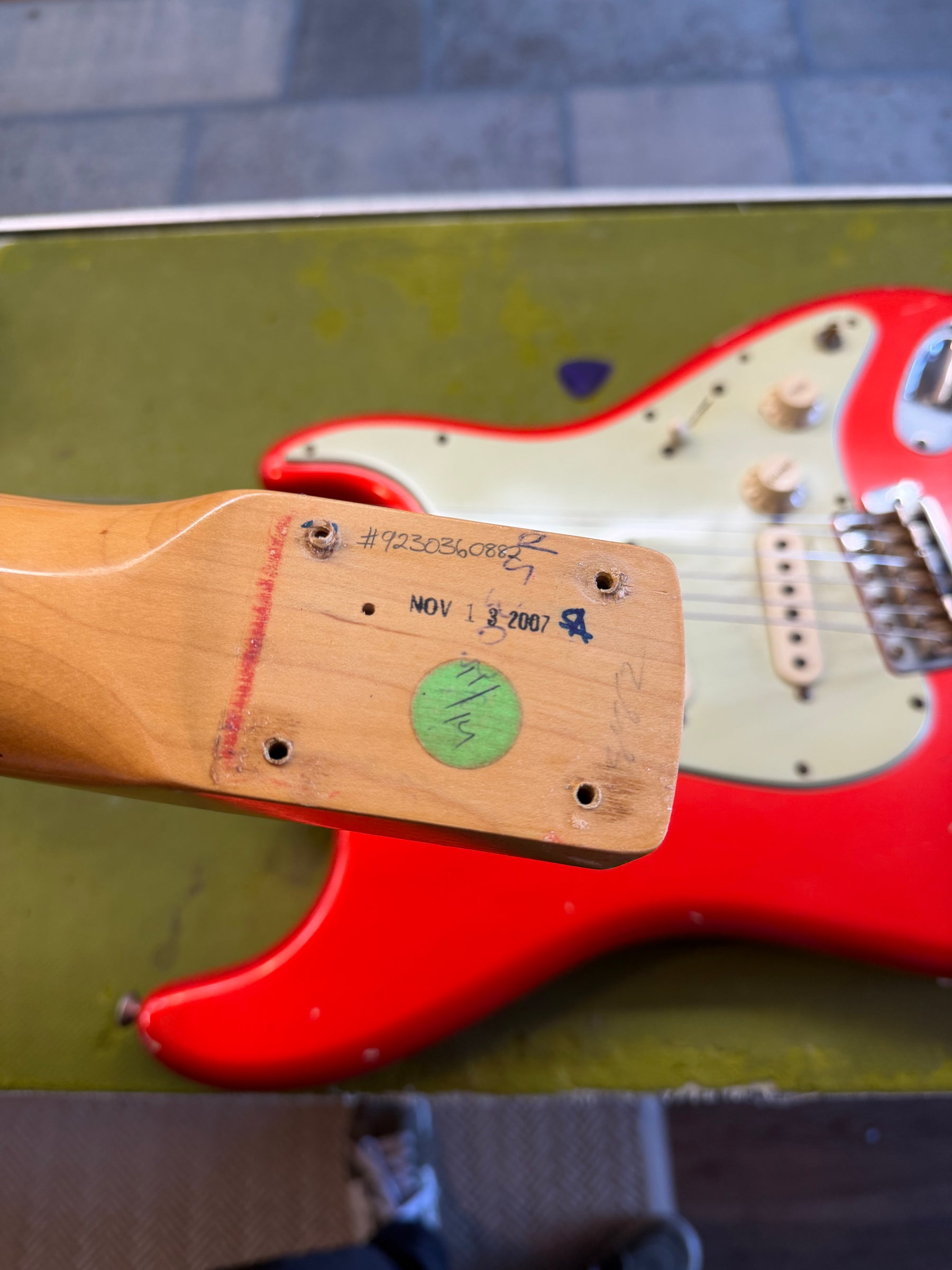 The guitar neck heel, with "NOV 13 2007" and a serial number, is detached from the Candy Tangerine body and white pickguard.