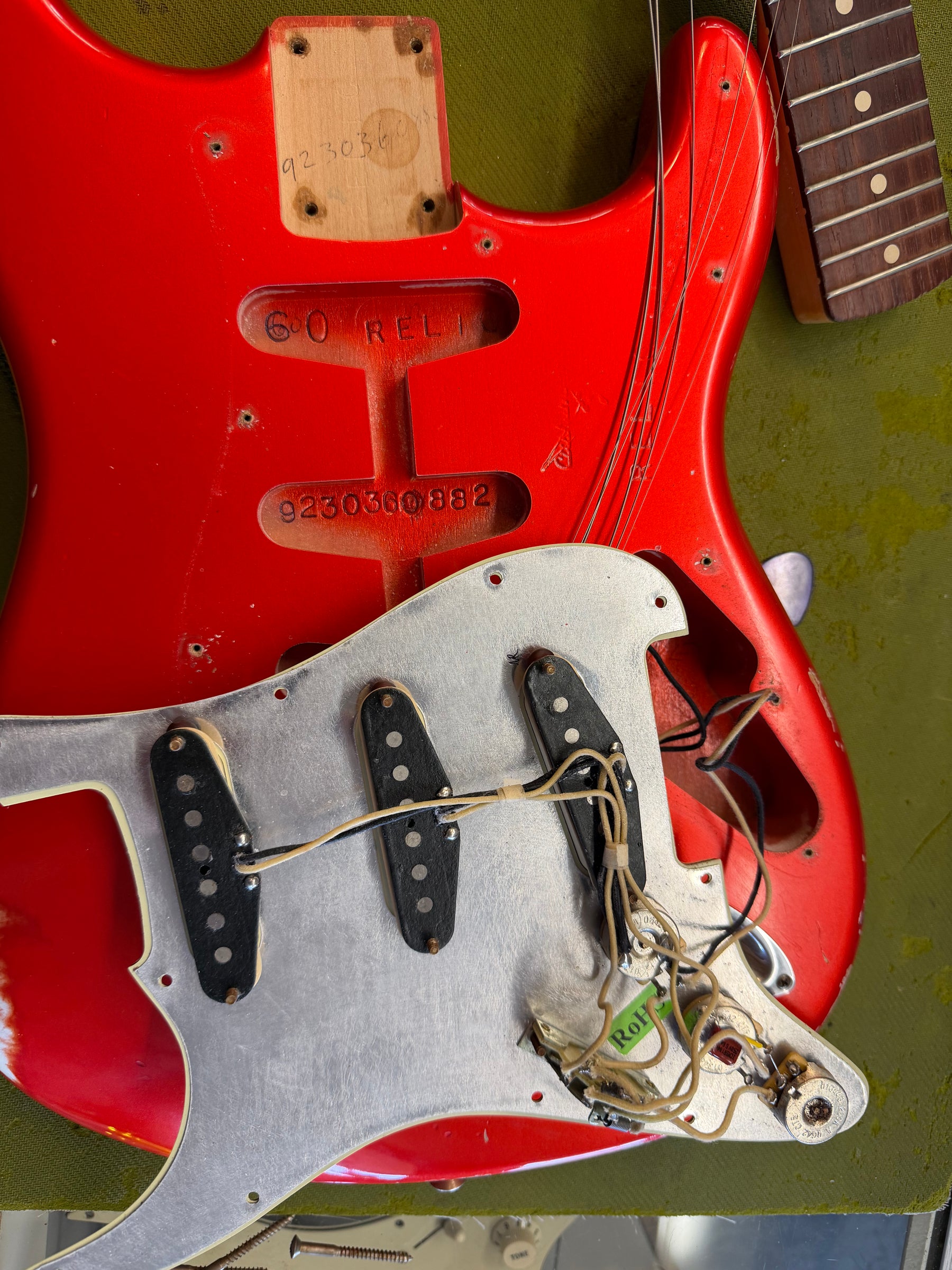 Overhead view of the red guitar body, with the pickguard removed to expose three single-coil pickups and wiring.