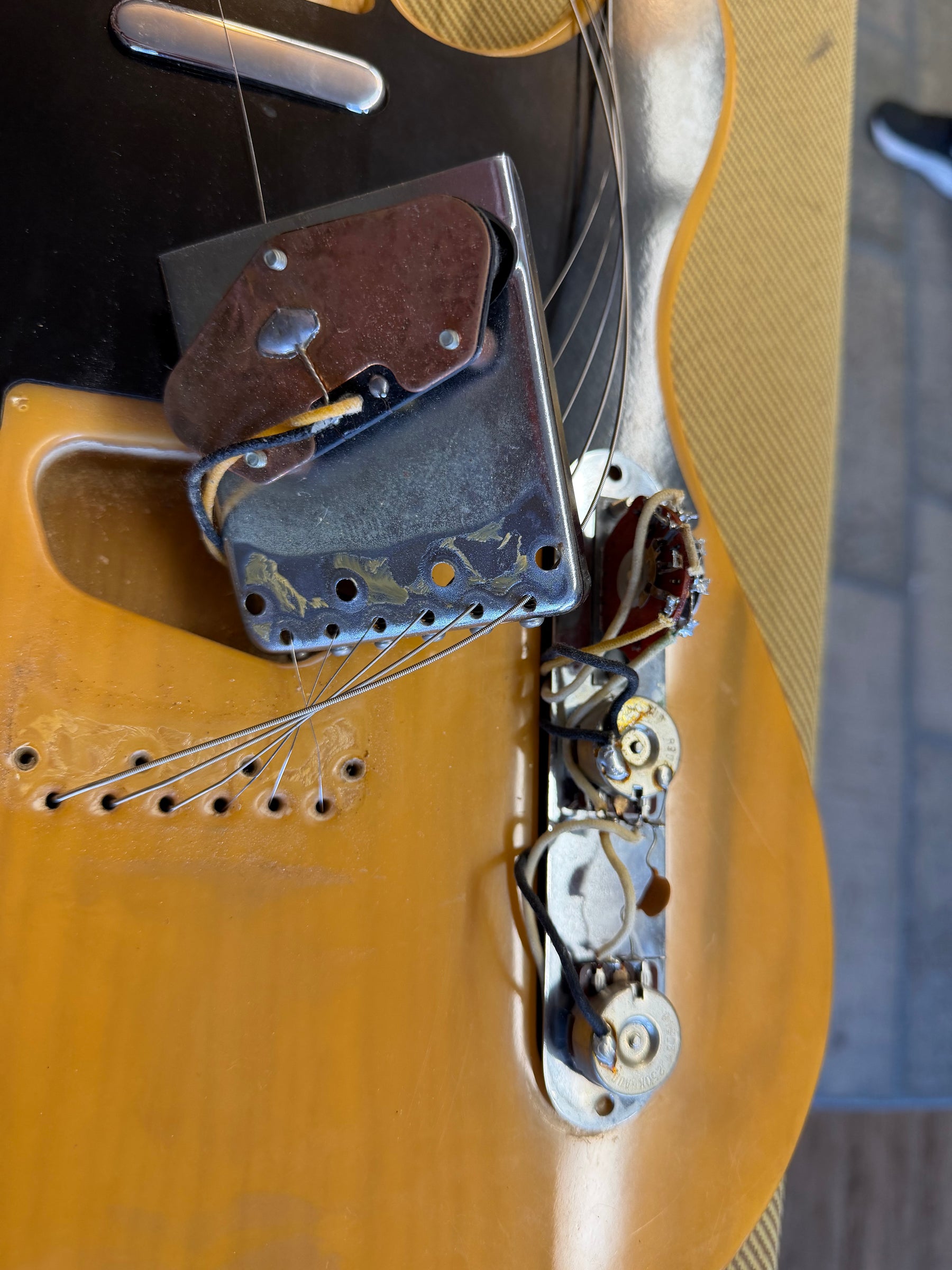 Close-up of the butterscotch blonde body, showing the bridge pickup, control plate with exposed wiring, and strings threaded through the body.