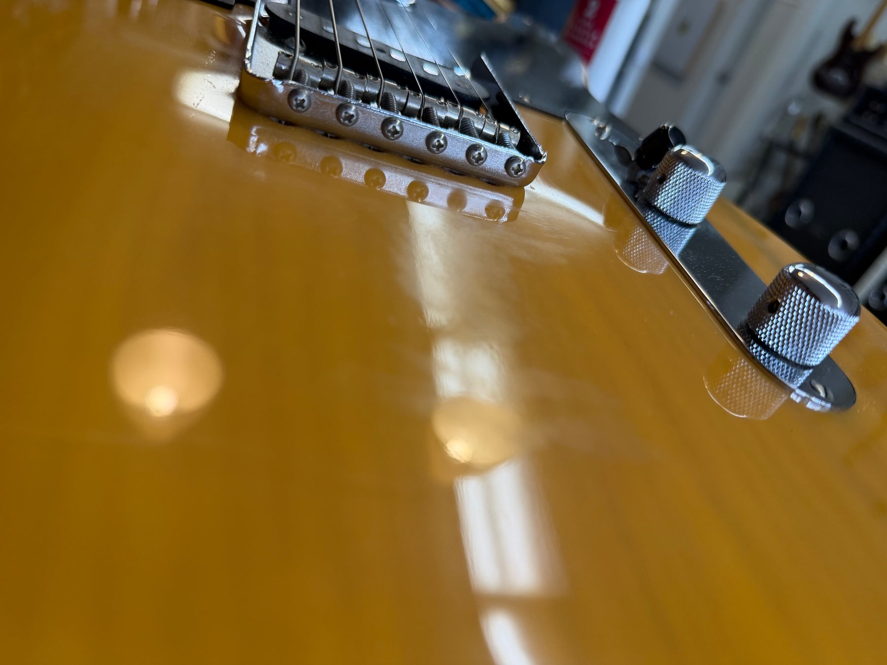 Close-up of a glossy butterscotch blonde Telecaster body, showing the chrome bridge and control plate with two knurled knobs.