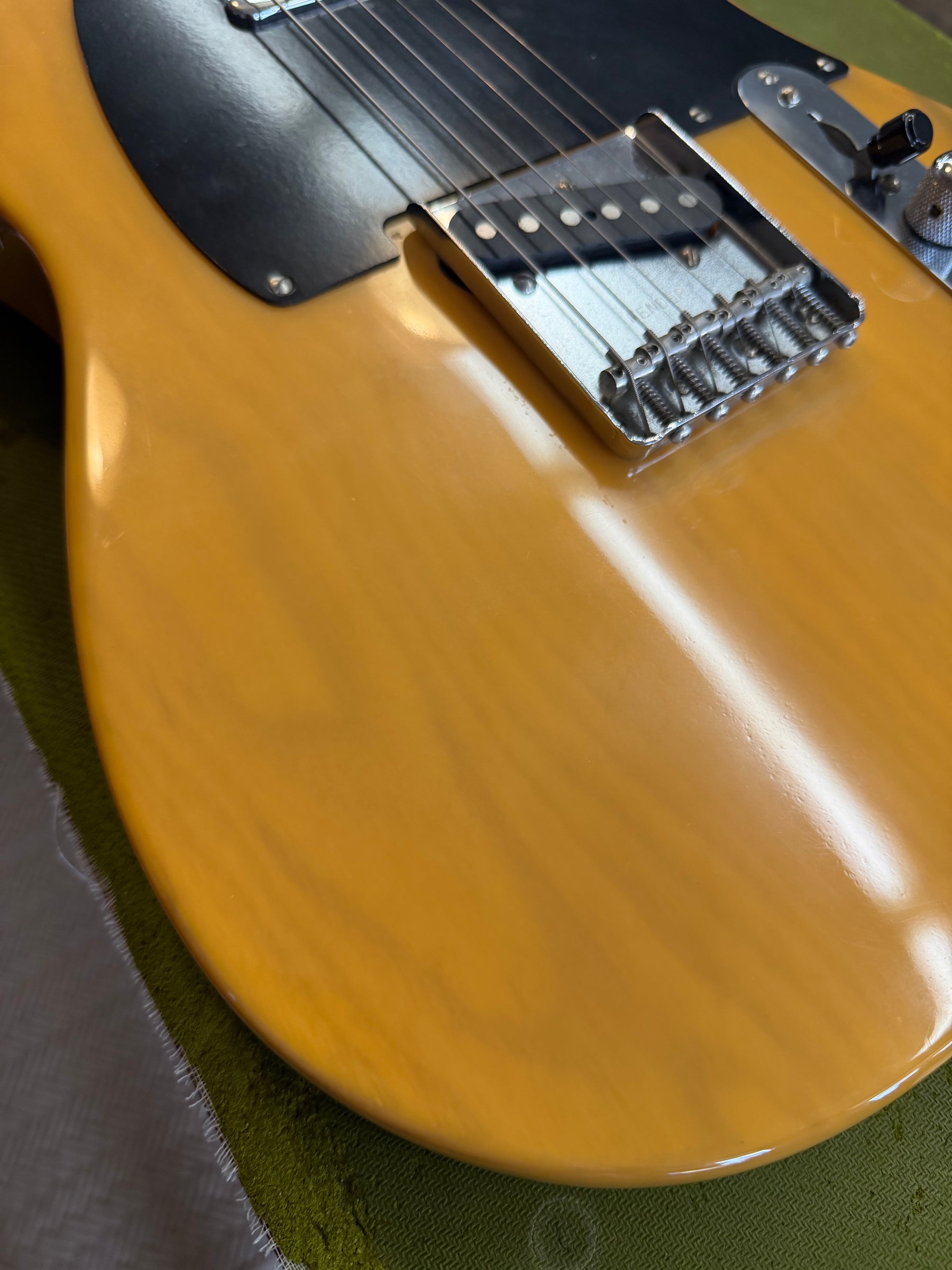 Close-up of the Telecaster's butterscotch blonde body, showing the black pickguard, chrome bridge, and subtle finish wear.