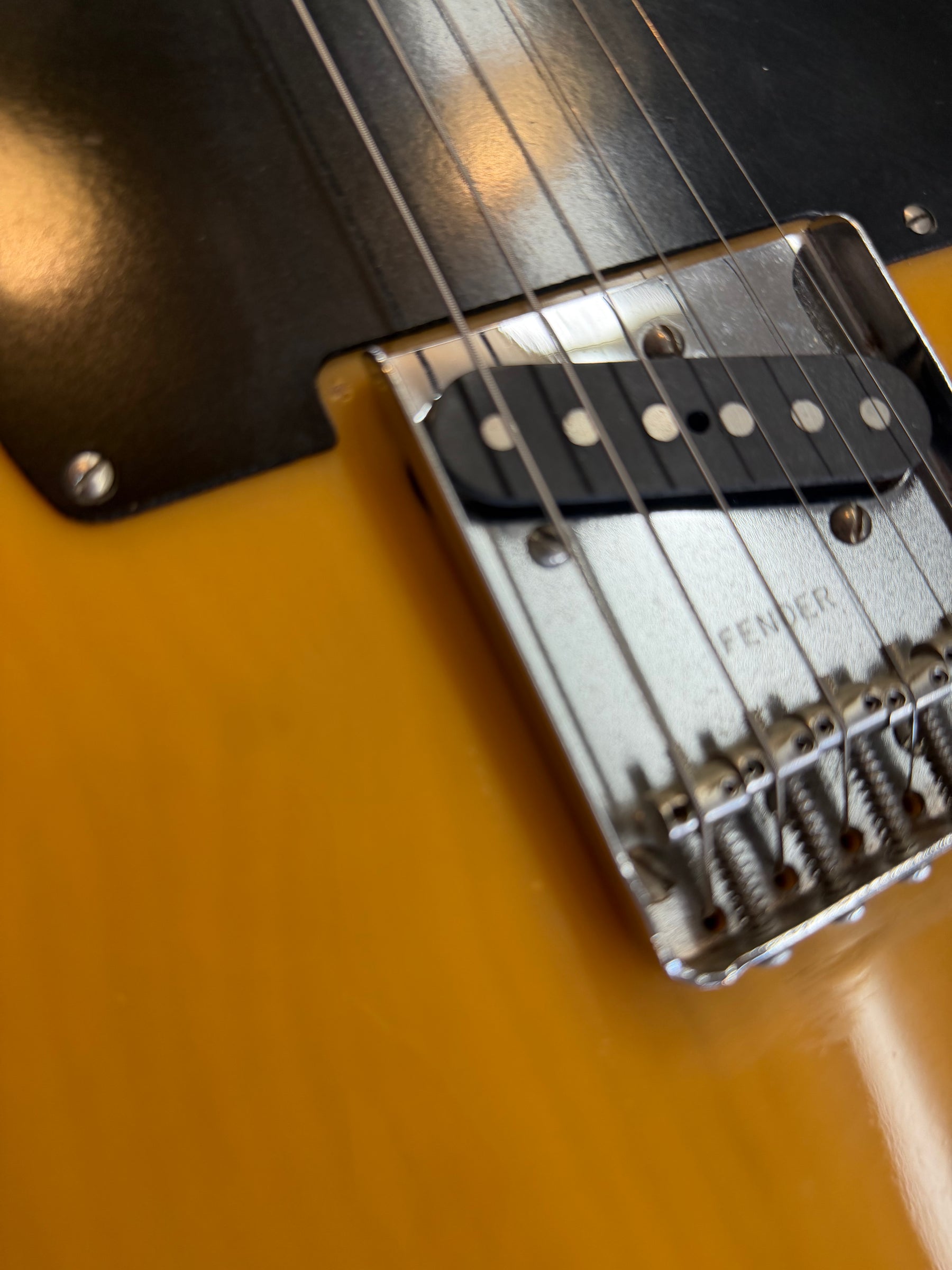 Close-up of the butterscotch blonde body, black pickguard, and chrome bridge with a single-coil pickup and six individual saddles.