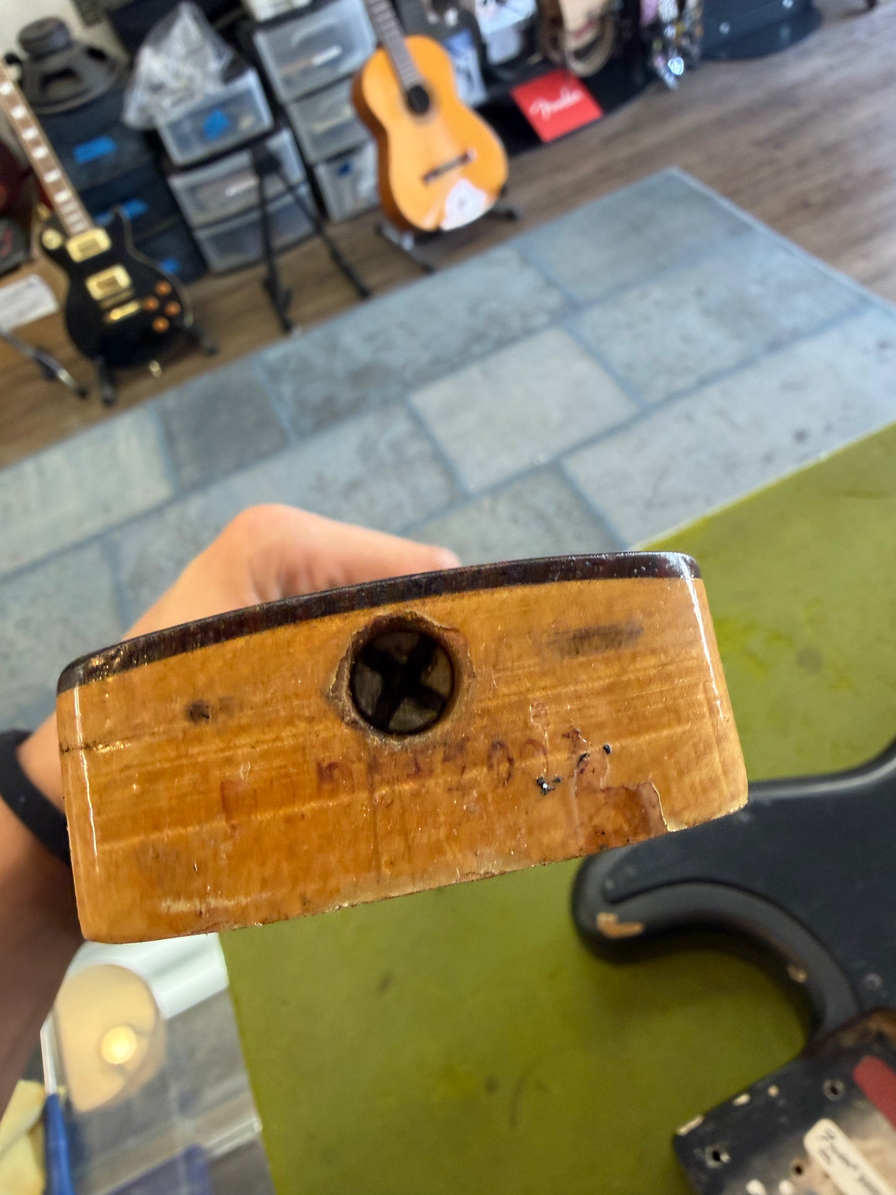 Close-up of the bass neck heel, showing a large truss rod adjustment screw, worn natural finish, and chipped wood.
