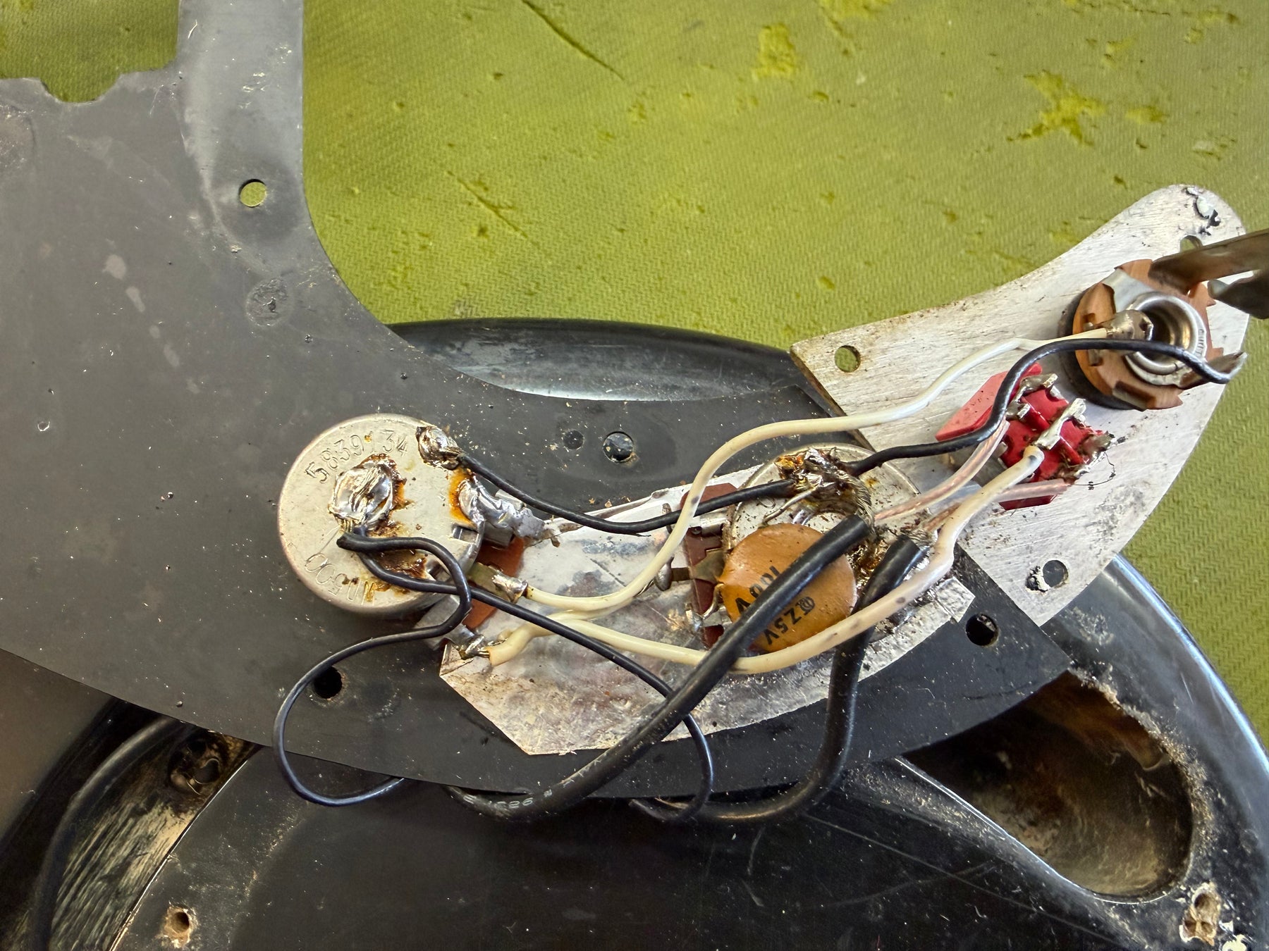 Close-up of the bass's control cavity, showing the wiring, potentiometers, and capacitor on the black pickguard.