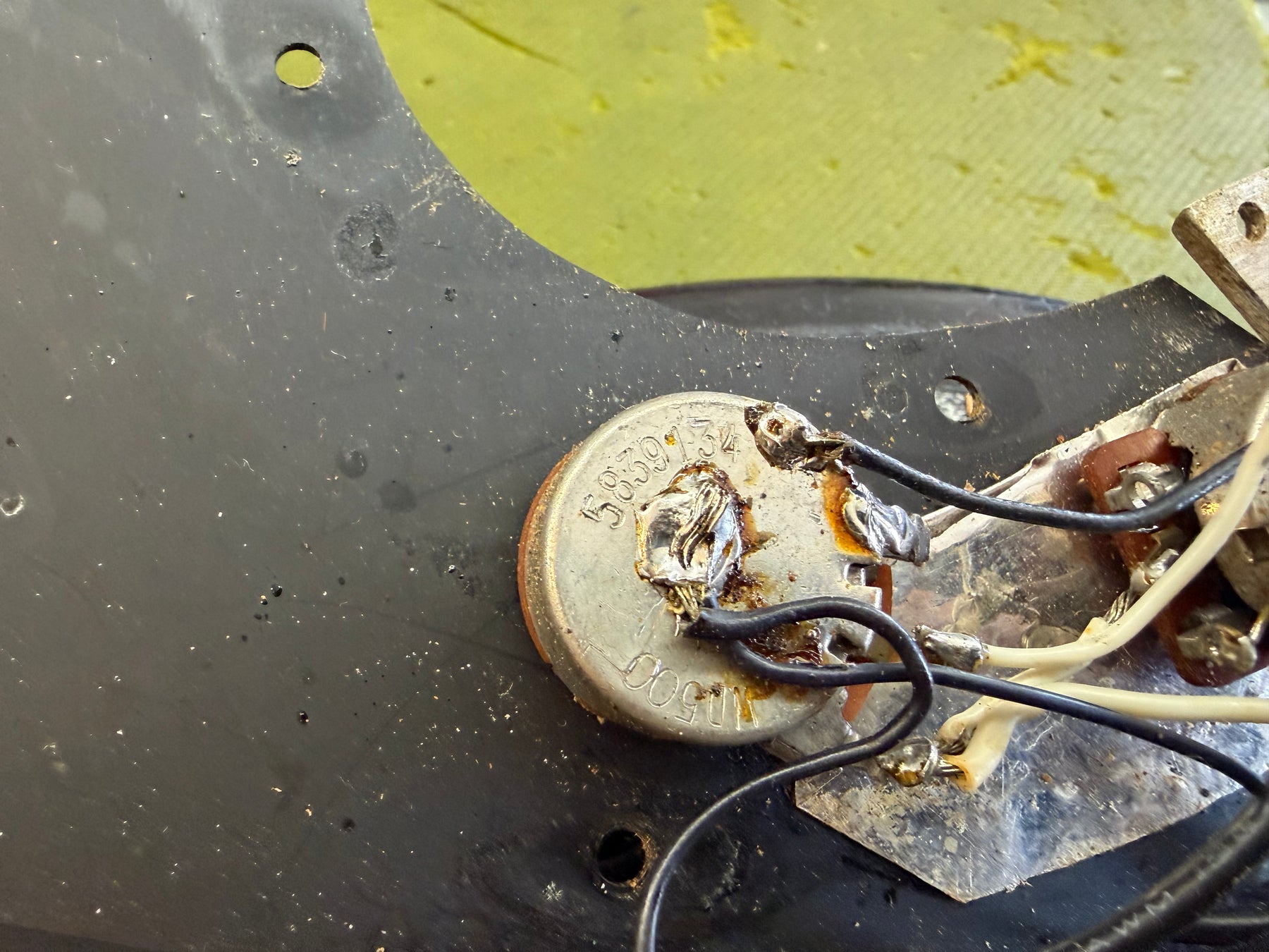 Close-up of the bass's internal electronics, showing a silver potentiometer with soldered wires and a black pickguard with dust and wear.