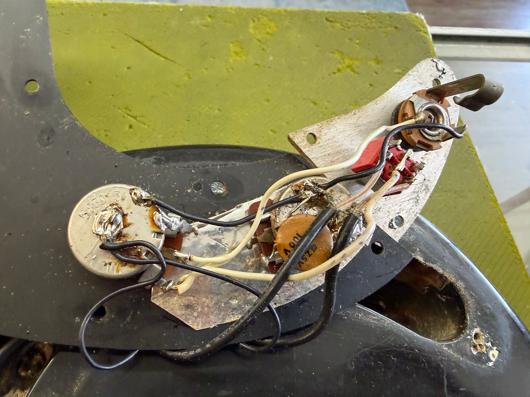 Close-up of the bass's exposed wiring cavity, showing two pots, a capacitor, and various wires on a worn metal plate.