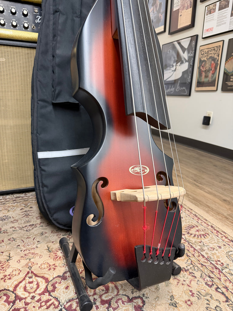 The upright bass, in a tobacco sunburst finish, is angled to show its f-holes, light wood bridge, and red strings.
