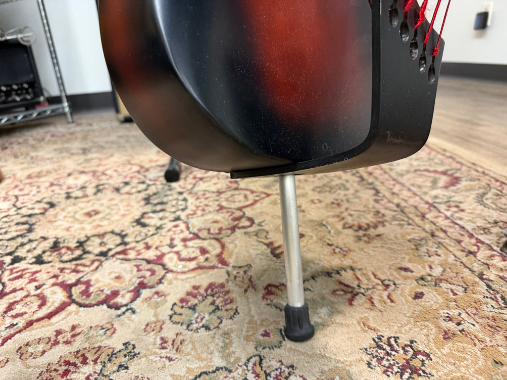 The bass's lower bout, in tobacco sunburst, rests on a single silver leg with a black rubber foot, viewed from below.