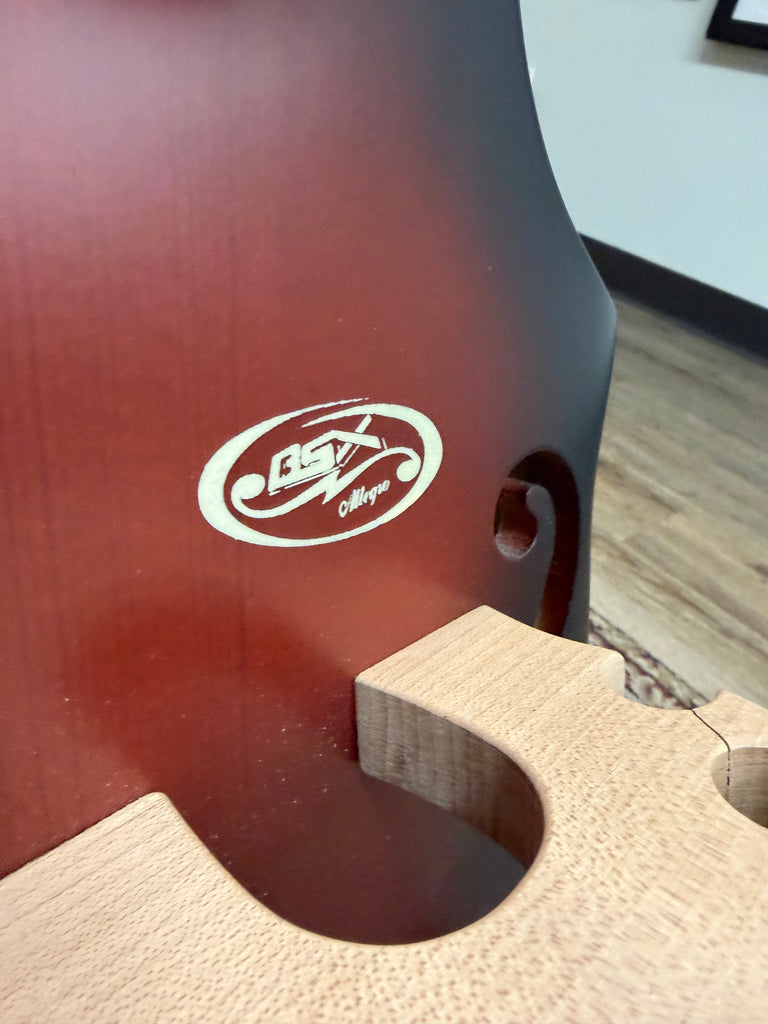 Close-up of the bass's tobacco sunburst body, showing a light-colored logo and a light wood bridge with a small crack.