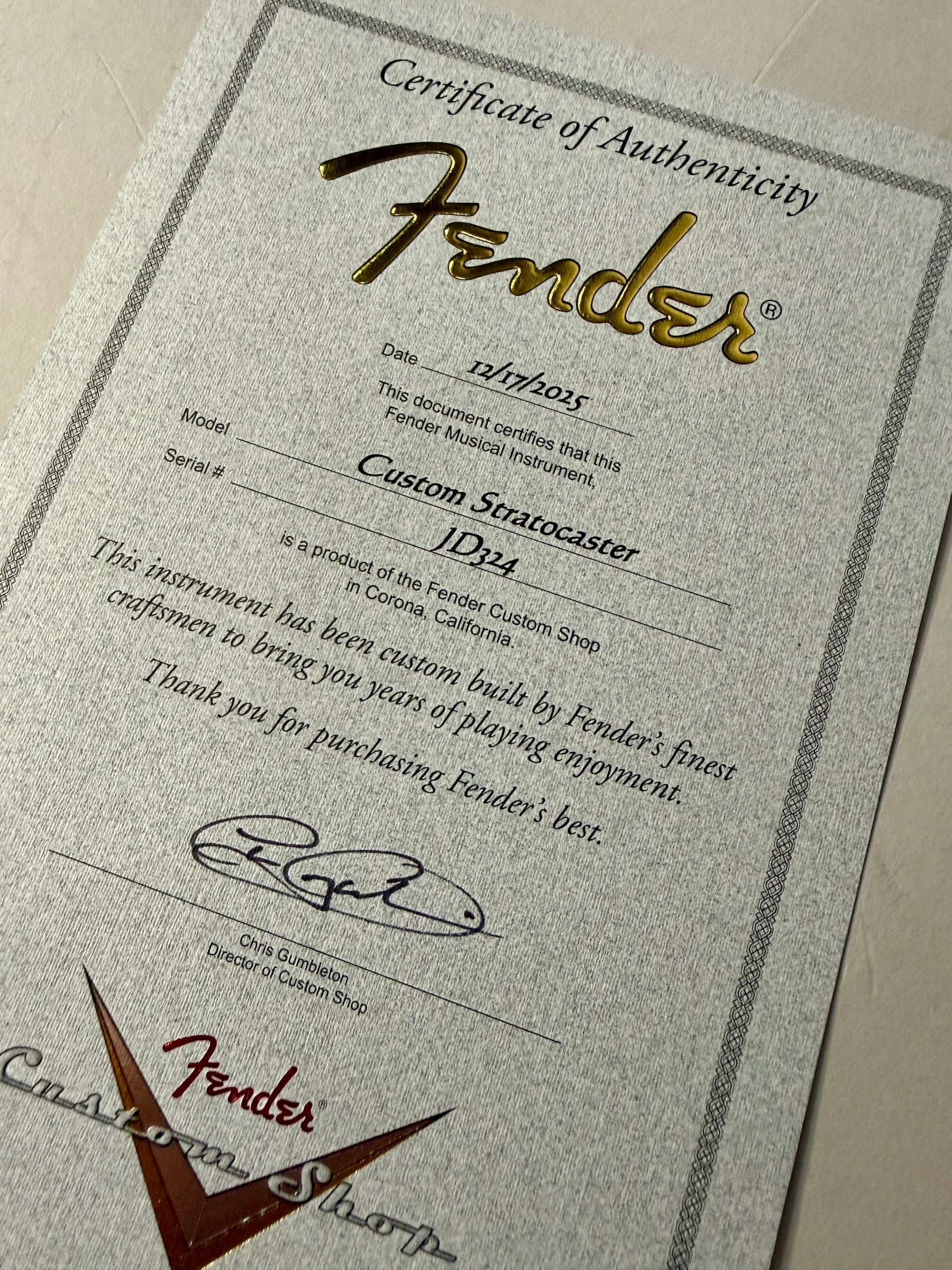 Close-up of the guitar's Certificate of Authenticity, showing "Custom Stratocaster" and "JD324" on textured gray paper.