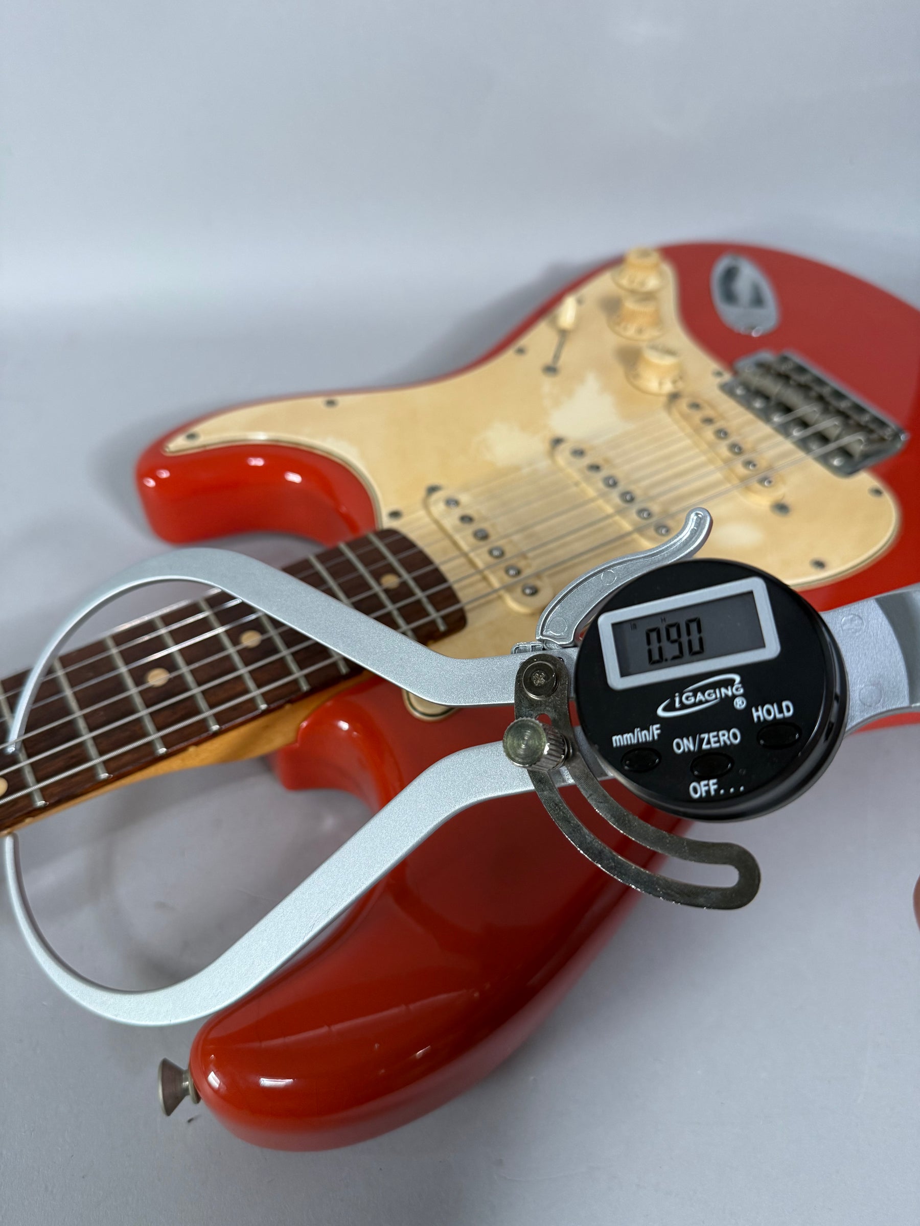 A Fiesta Red Stratocaster body and neck, with a digital caliper measuring the fret height at 0.90, showing light wear on the pickguard.