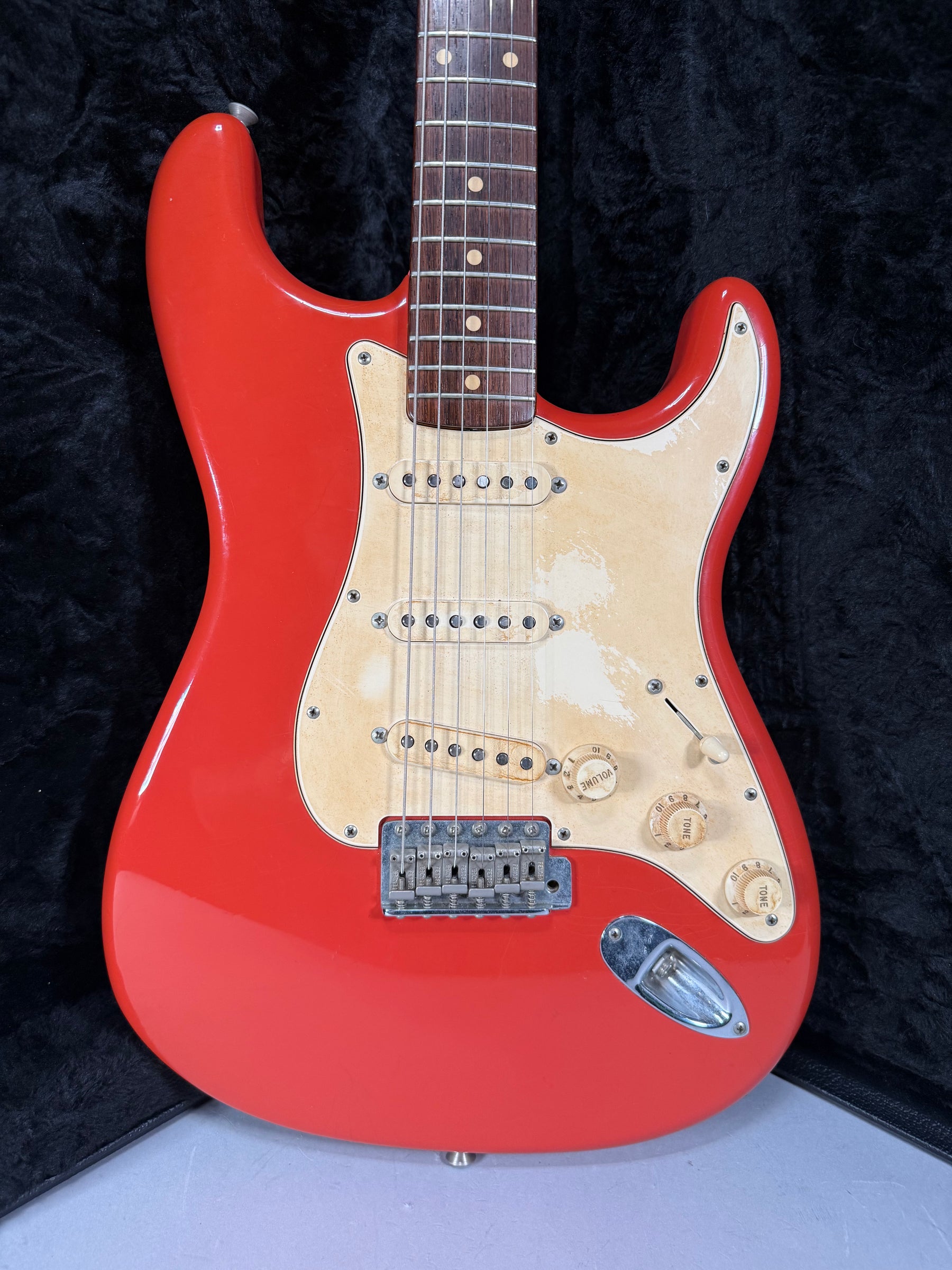 Full view of a Fiesta Red Stratocaster with a worn, aged cream pickguard, three single-coil pickups, and a chrome tremolo bridge.