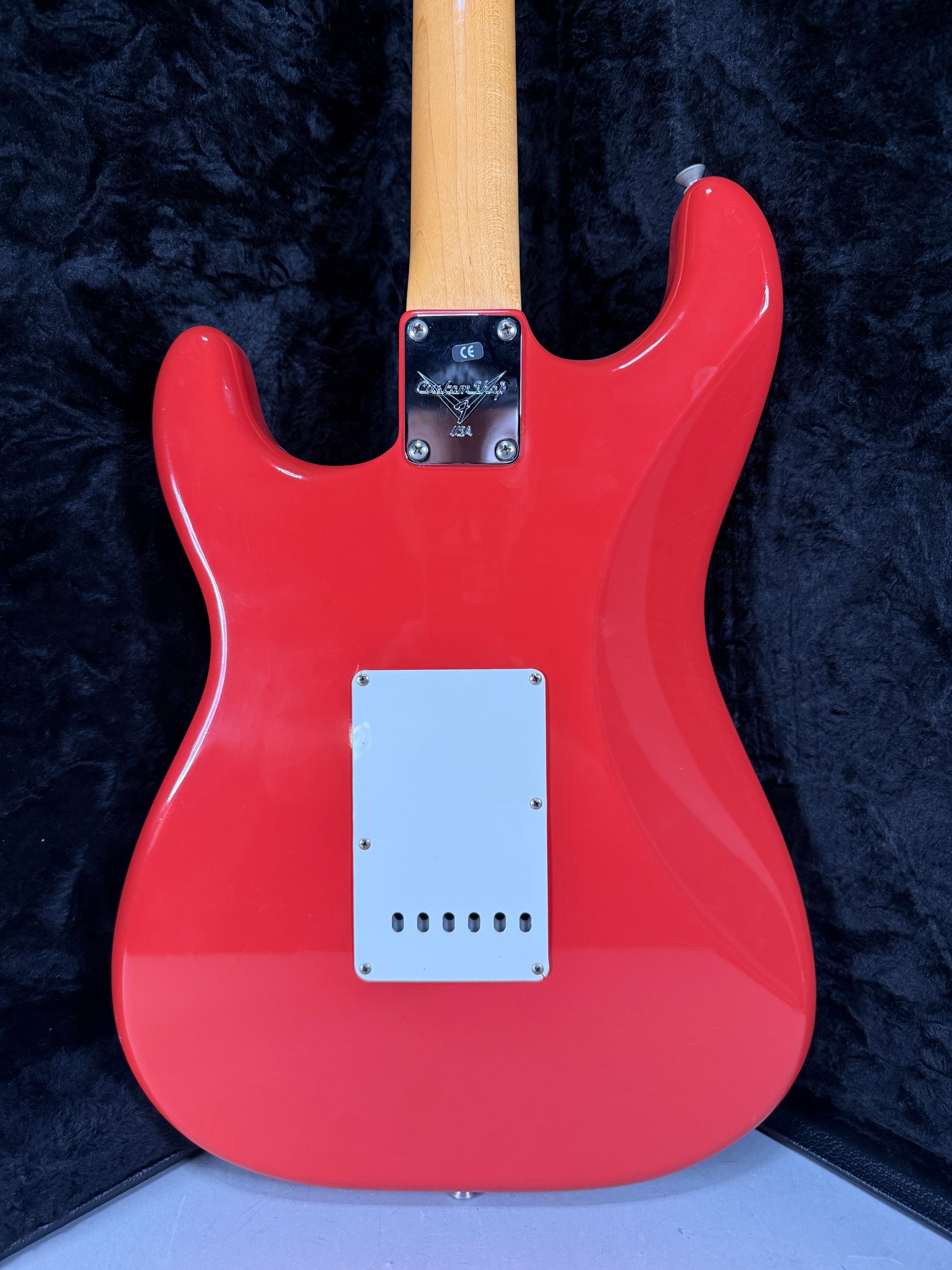 The back of a glossy red Stratocaster, showing the neck plate, a light gray tremolo cover, and a light-colored maple neck.
