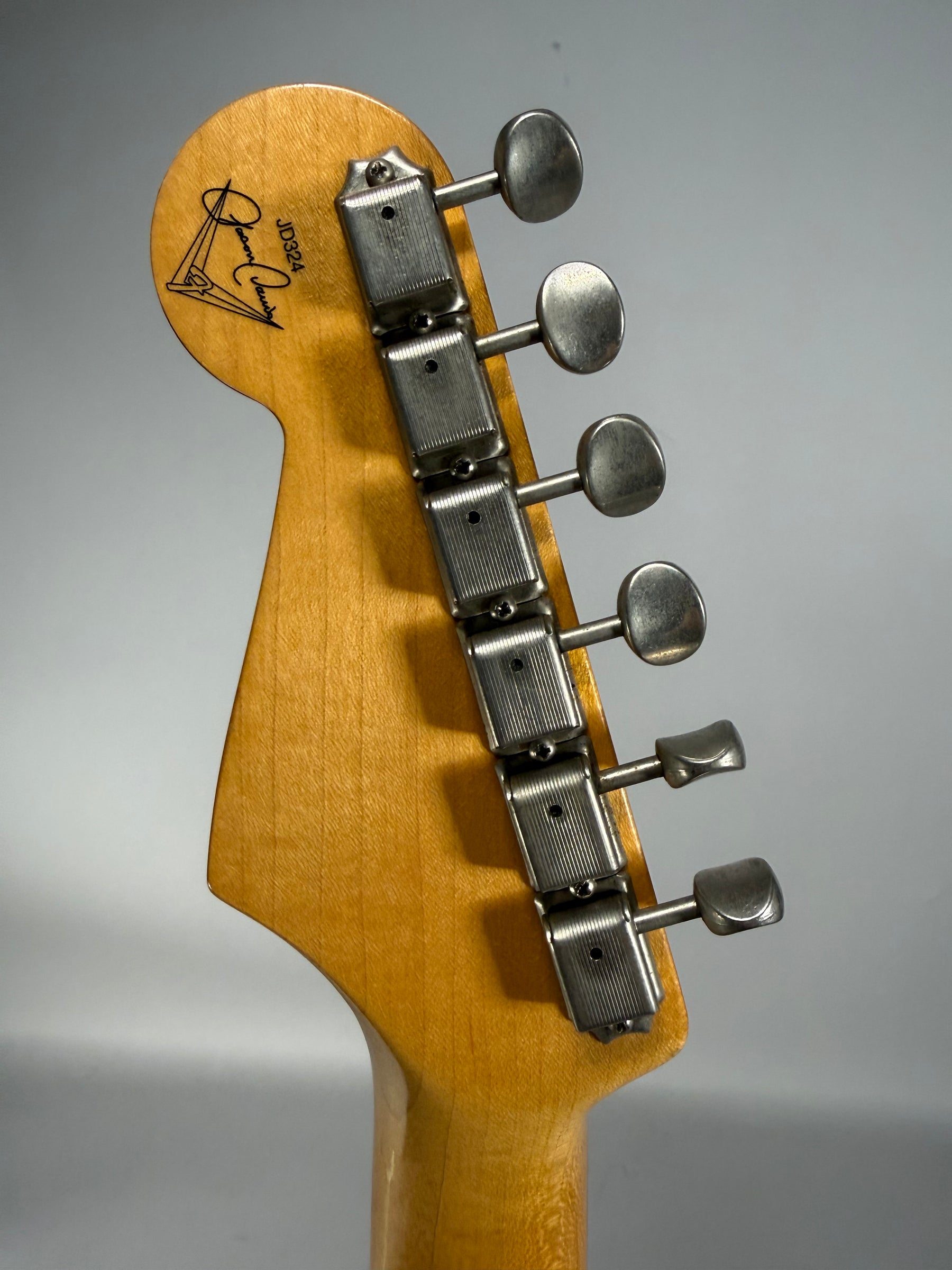 The guitar's headstock, angled slightly left, shows a light wood finish, six aged silver tuners, and a black signature logo.