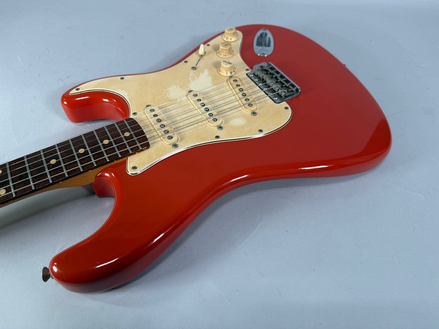 Fiesta Red Stratocaster body and neck, angled from the lower bout, showing the aged cream pickguard, three single-coil pickups, and tremolo bridge.