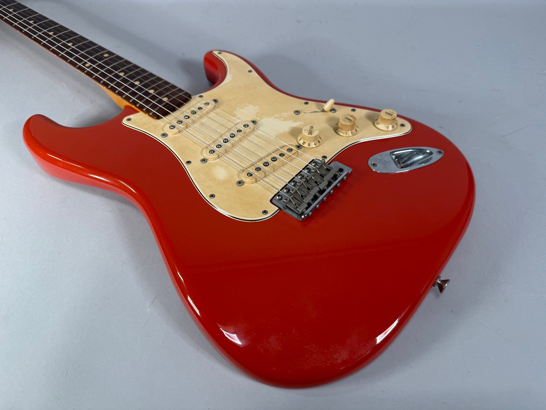 Fiesta Red Stratocaster body and lower neck, showing a worn cream pickguard, three single-coil pickups, and chrome hardware.