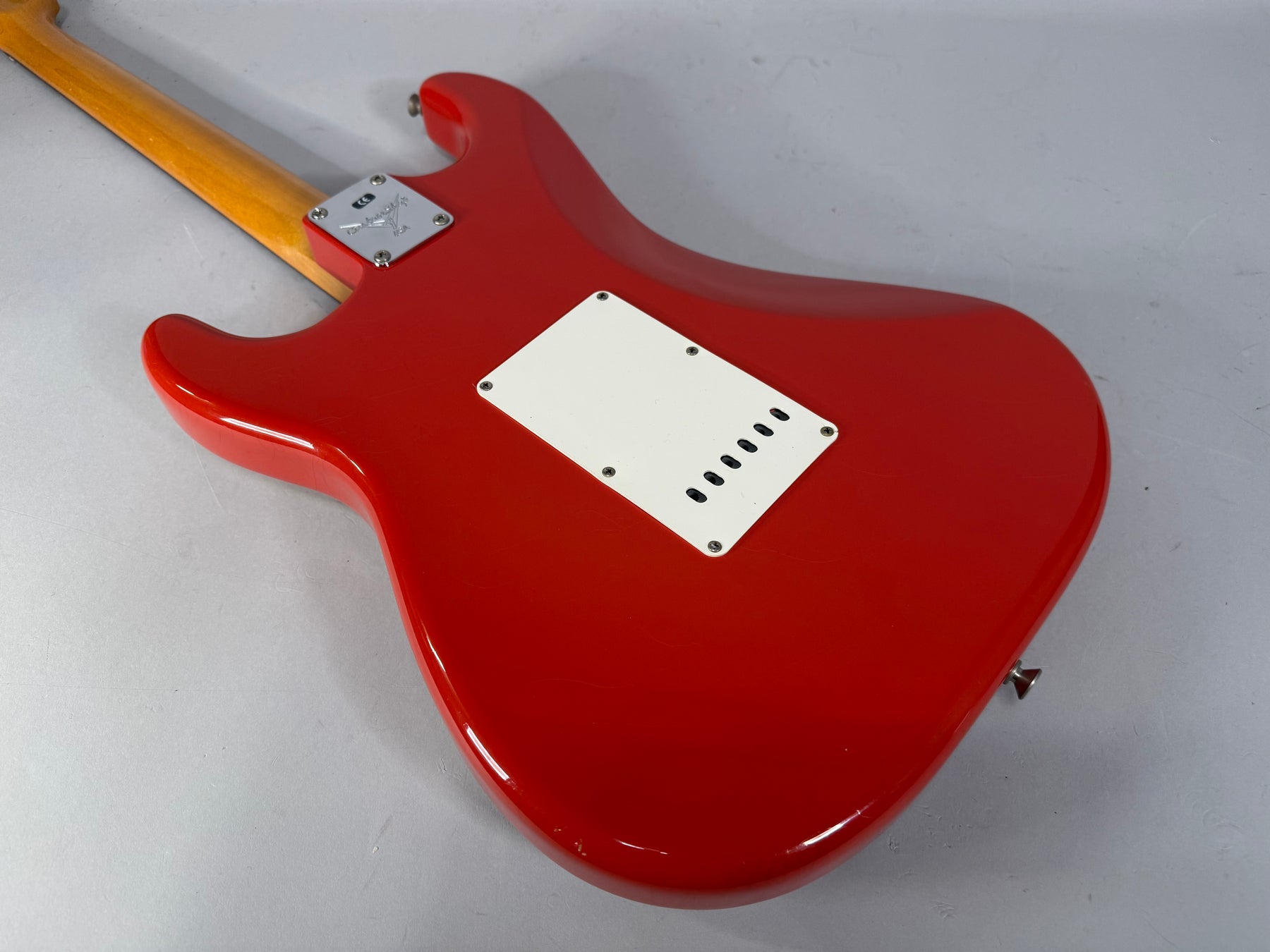 The back of a glossy red Stratocaster, angled from the neck to the lower bout, showing a white tremolo cover and chrome neck plate.