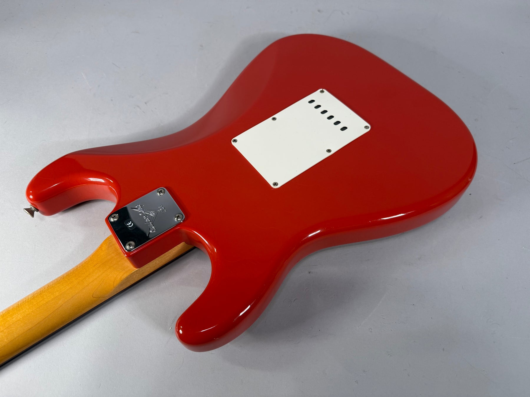 The back of a glossy Fiesta Red Stratocaster body, angled right, shows a white tremolo cover and a chrome neck plate.