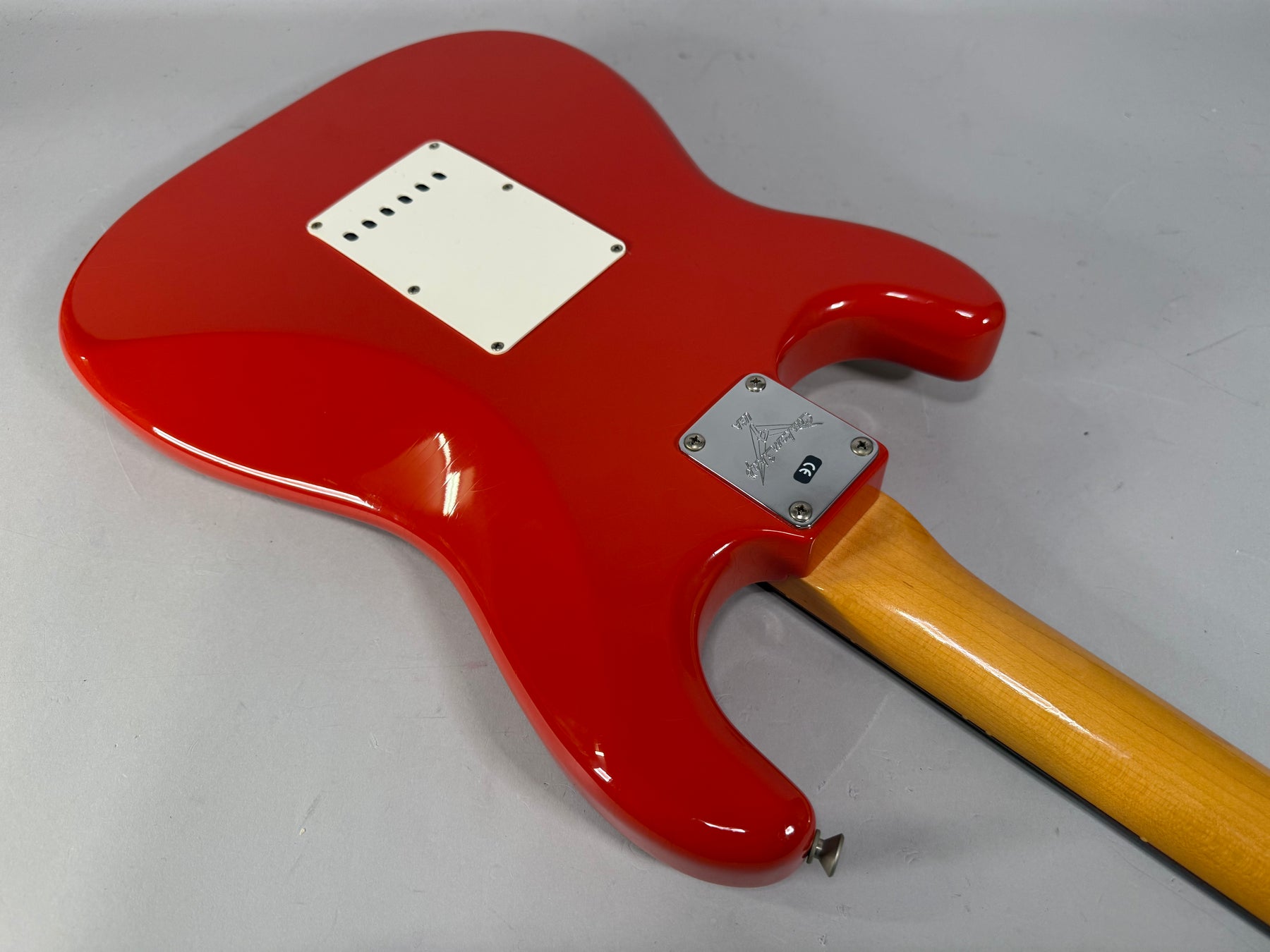The Fiesta Red Stratocaster's glossy back, with a white tremolo cover and chrome neck plate, shows light wear on the lower bout.