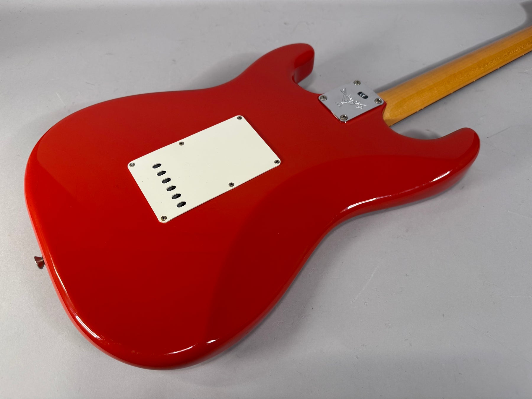 The back of a glossy Fiesta Red Stratocaster body, angled from the lower left, with a white tremolo cover and chrome neck plate.