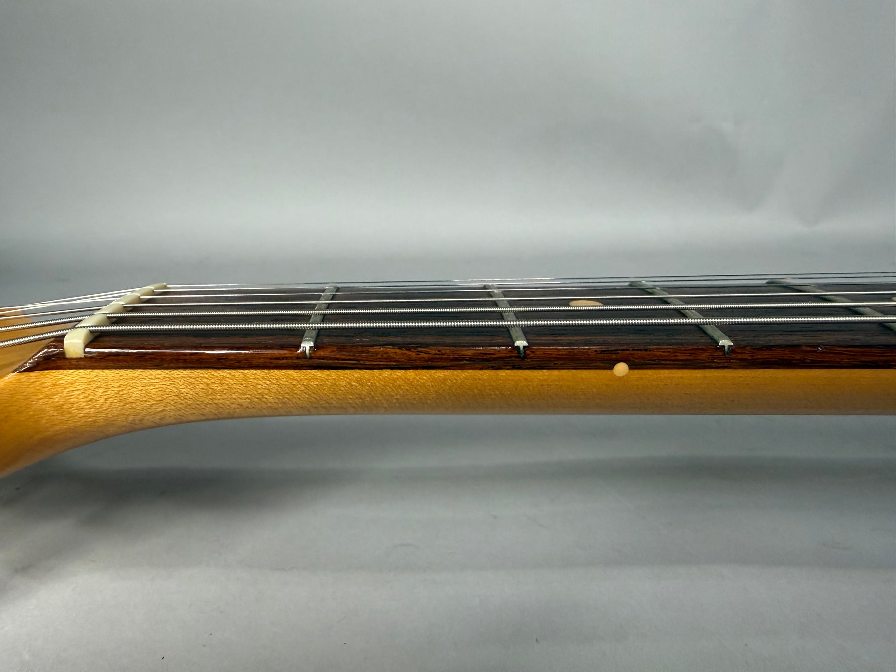 The guitar's neck, with a dark rosewood fretboard, light maple neck, and a small ding on the lower edge.