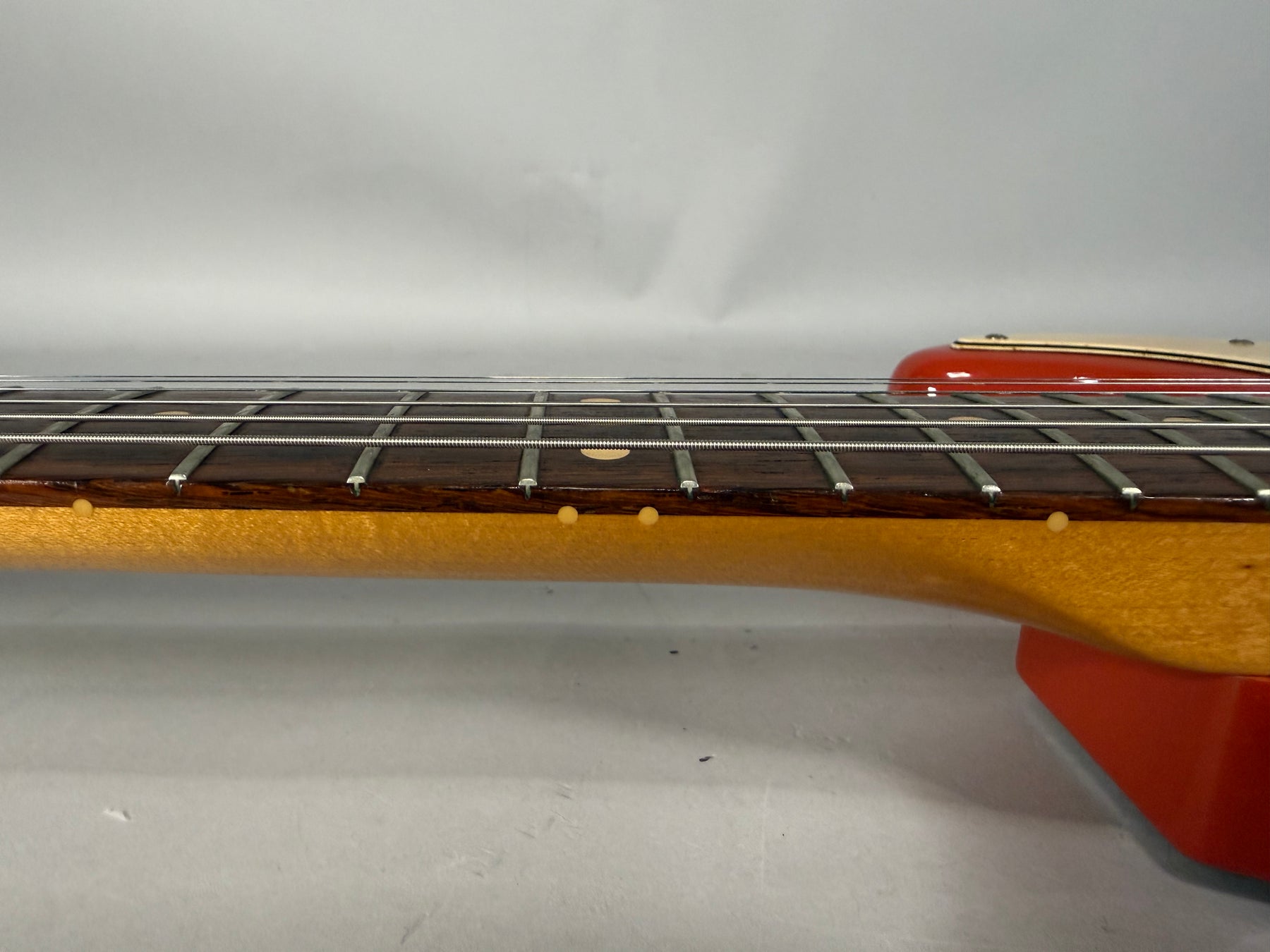 The guitar's neck and fretboard are viewed from the side, showing the dark wood fretboard with light dot inlays and a maple neck.