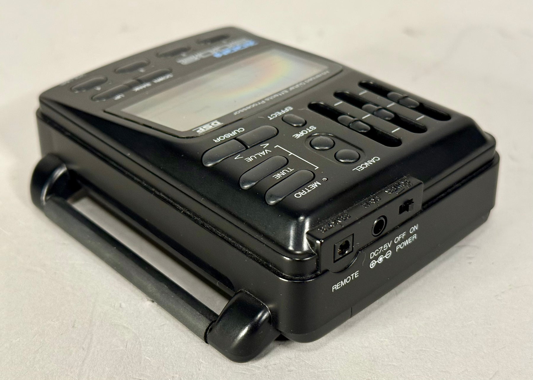 A black effects processor, angled from the right, showing its screen, control buttons, and the power/remote input panel.