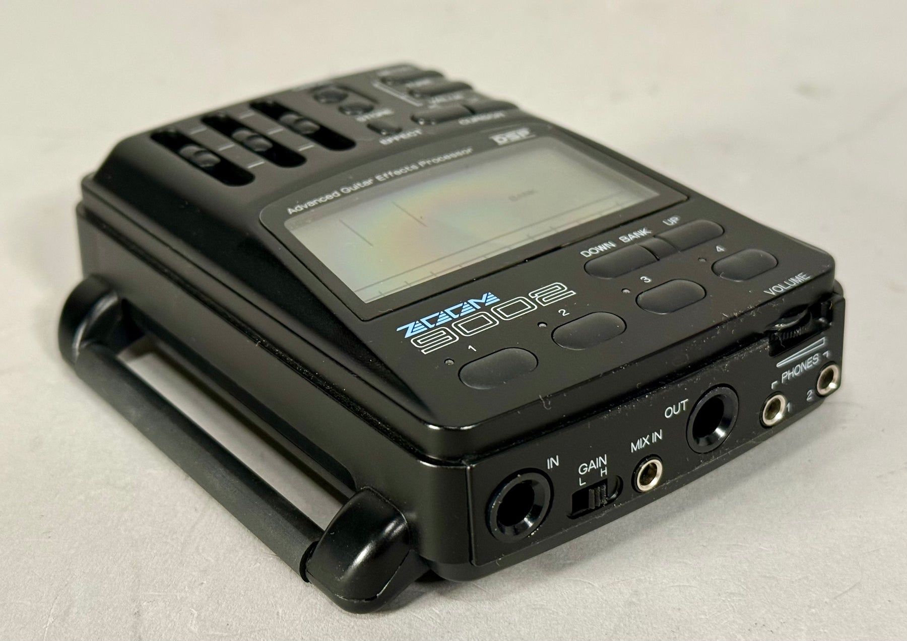 Black effects processor, angled from the right, showing the top panel with sliders and screen, and the front panel with jacks and a gain switch.