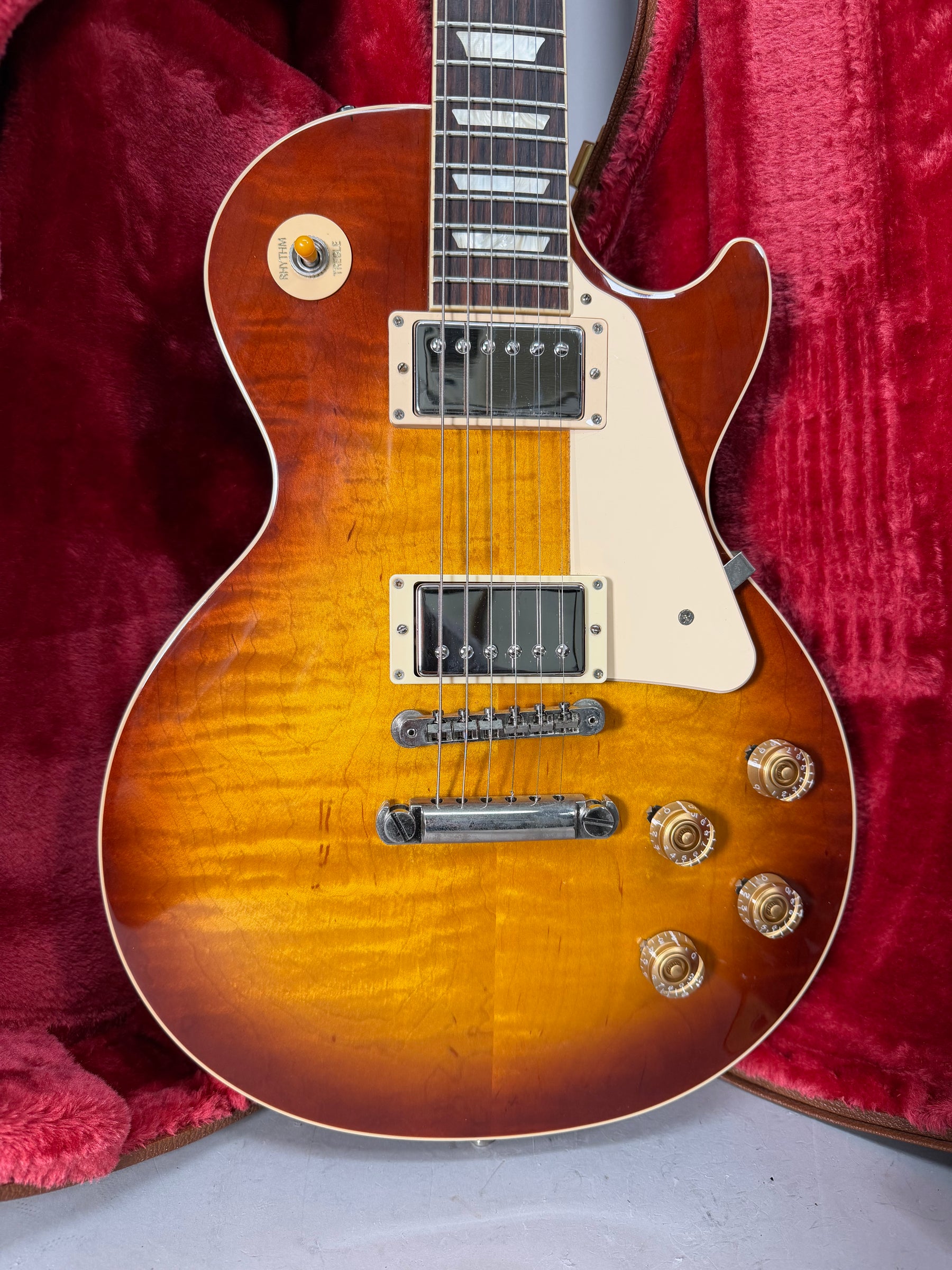The Les Paul's Iced Tea Burst body, with visible flame maple grain and light wear, is framed against a red plush case.