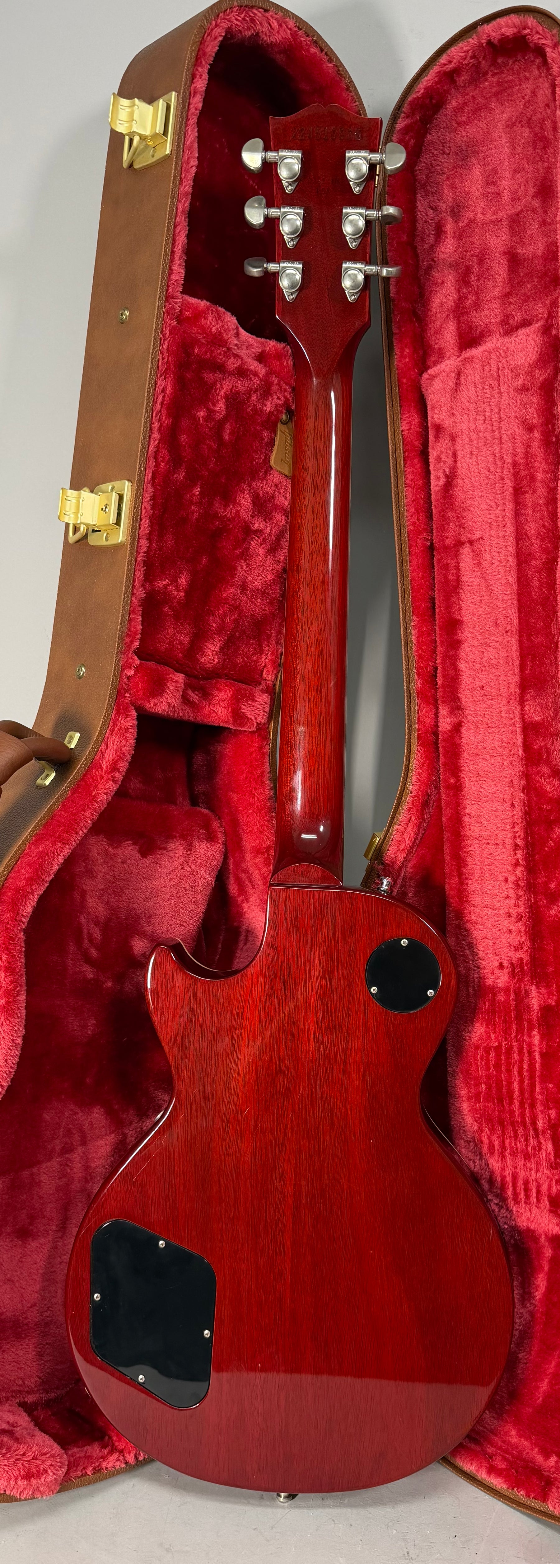 The back of a glossy, dark red guitar with a matching headstock, silver tuners, and black control plates, resting in a red plush case.