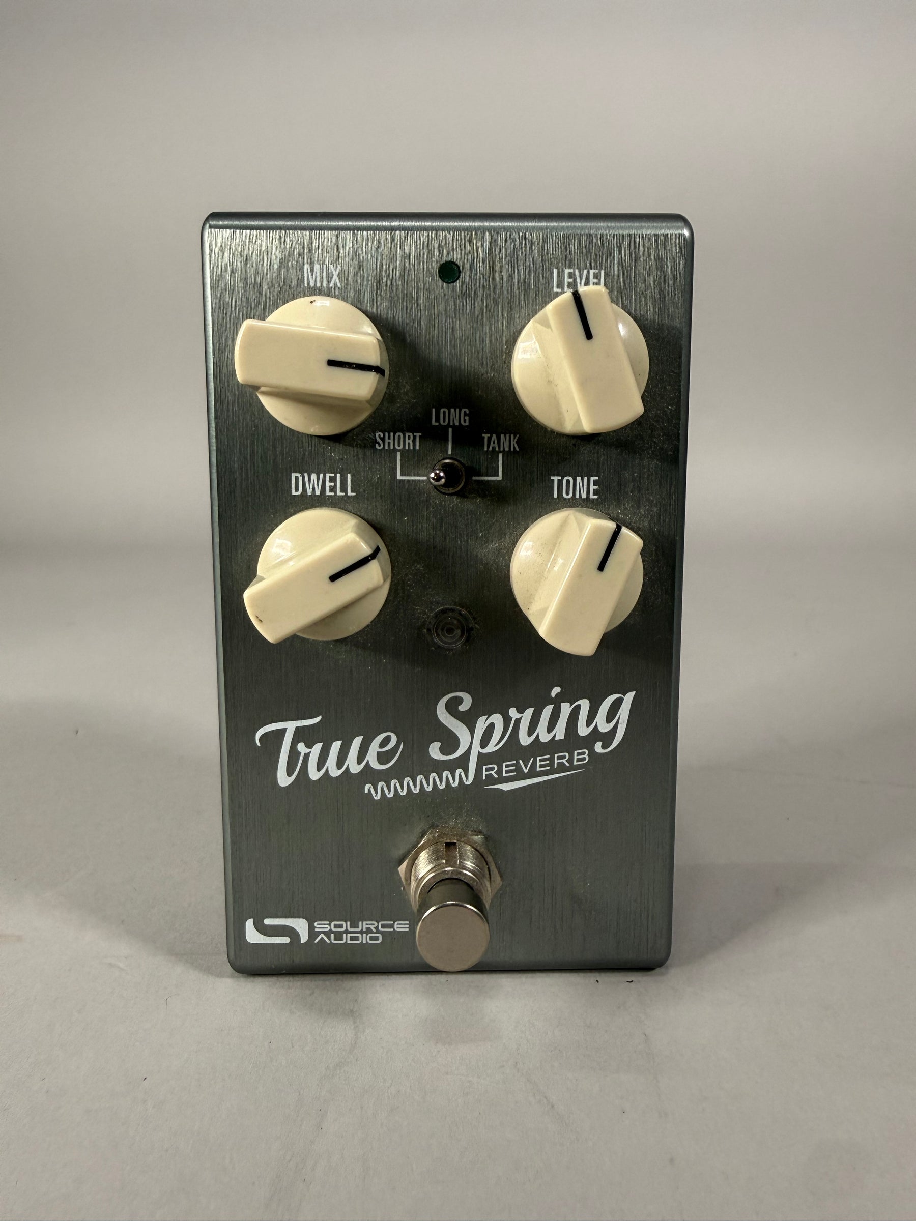 A top-down view of the brushed dark grey pedal with four cream-colored knobs, a small toggle switch, and a silver footswitch.