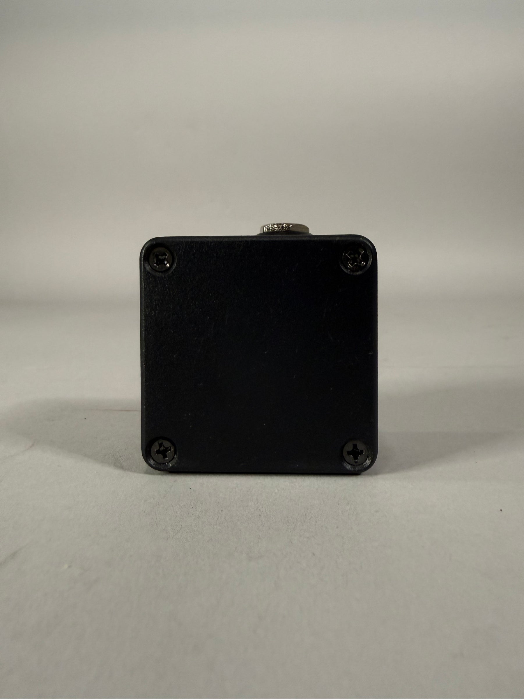 The black pedal's rear is visible, showing four corner screws and a single silver jack at the top center.