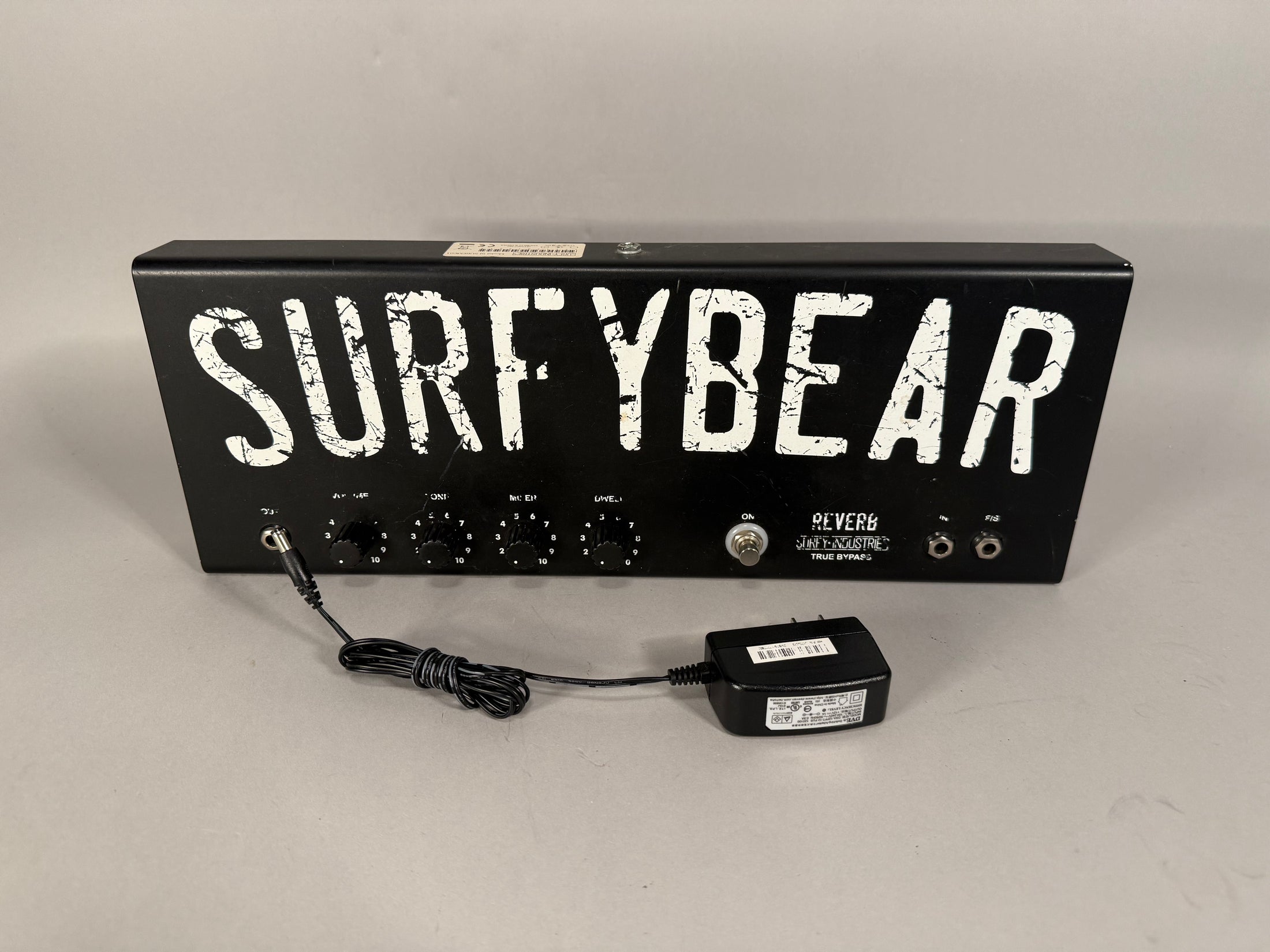 Black metal reverb unit with distressed white lettering, five black knobs, a toggle switch, and two input jacks.