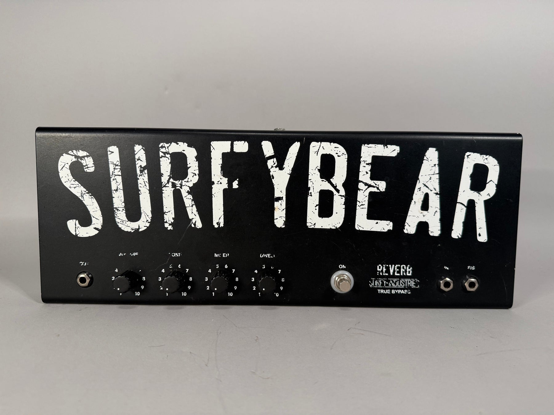 Black metal reverb unit, front view, with four black control knobs, a chrome toggle switch, and three input jacks.